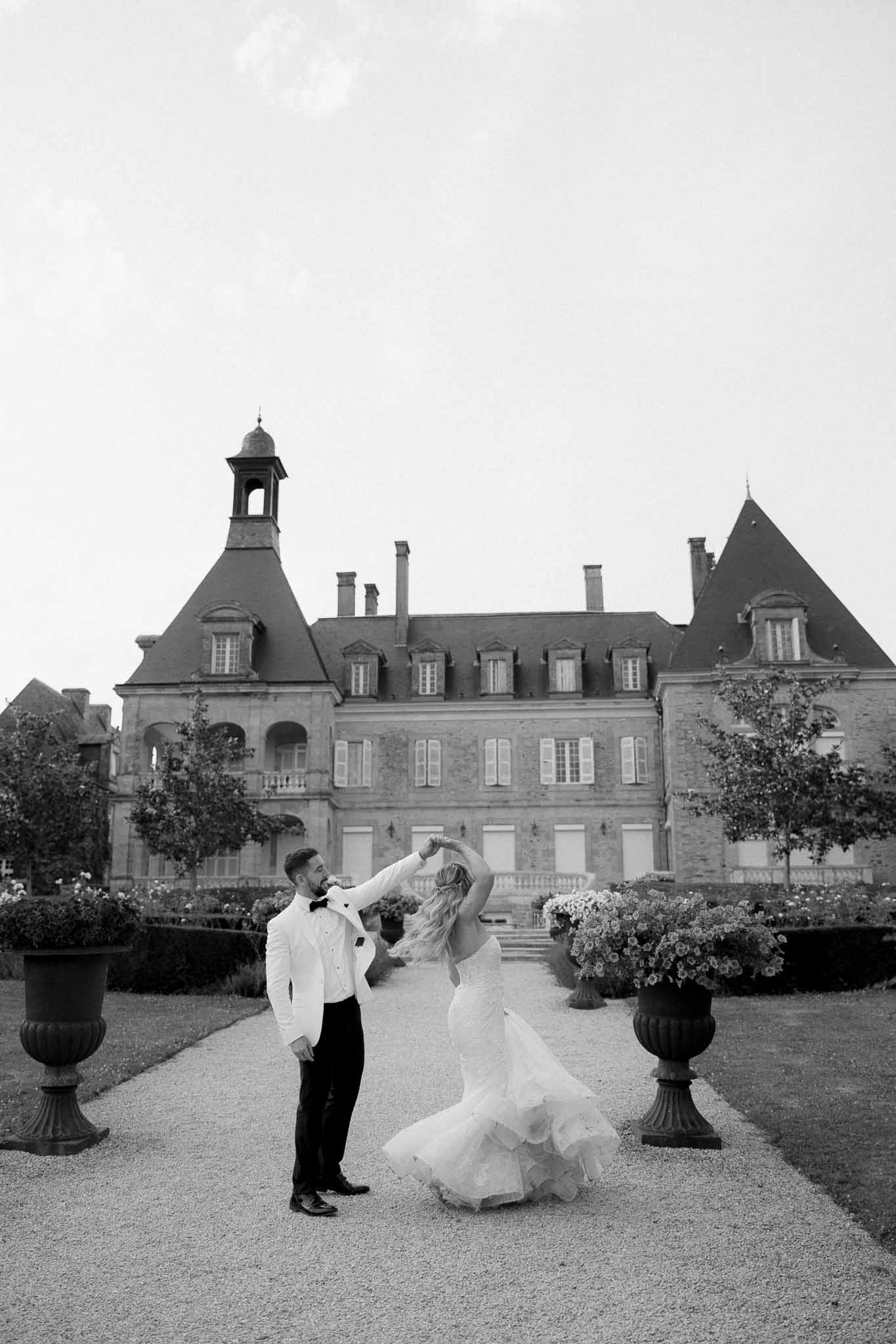 Bride and groom dancing in formal courtyard of French château with stone architecture and manicured gardens