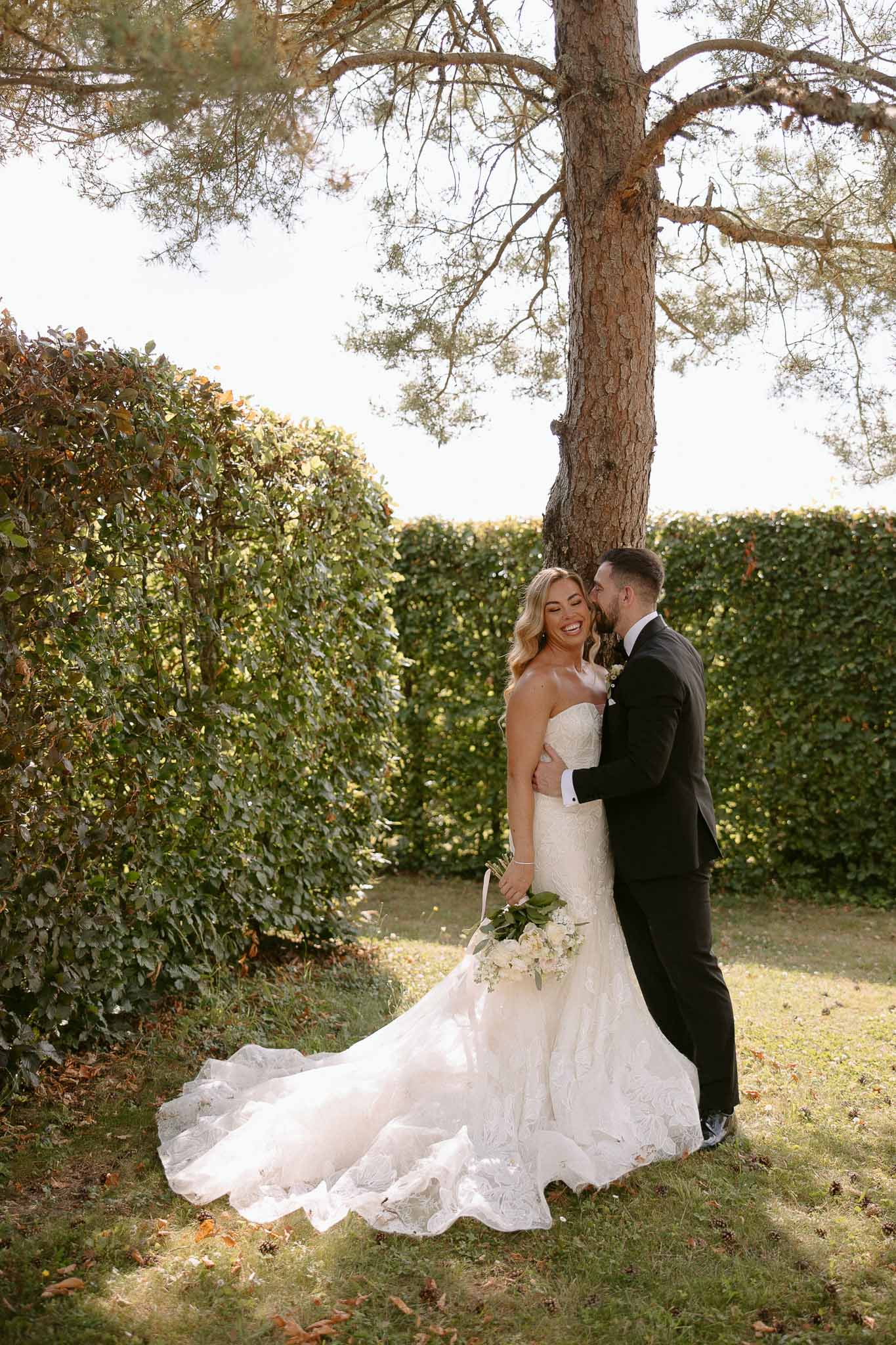 Bride and groom formal portrait in manicured garden with mature tree and hedges