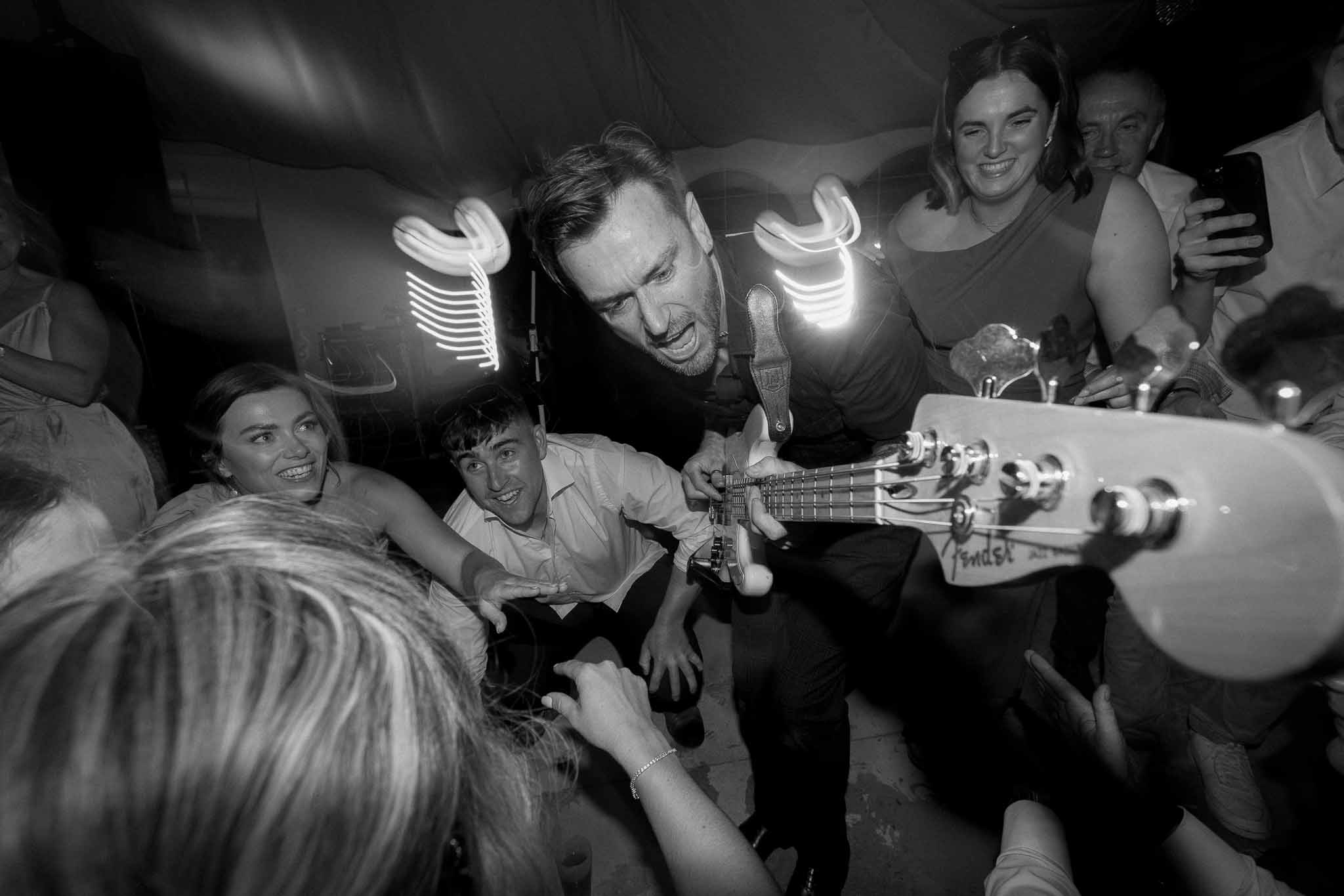 Black and white photo of guitarist playing electric guitar among cheering wedding guests in a marquee