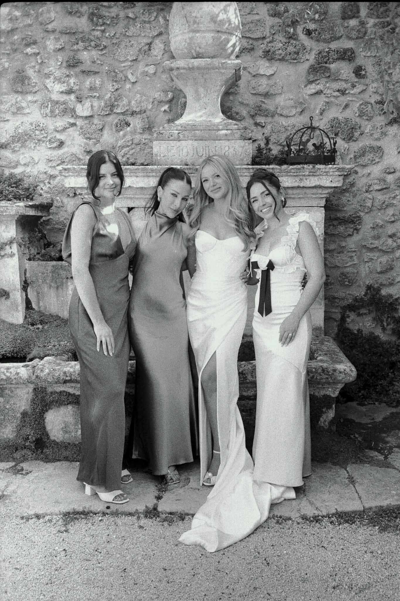 Bride and bridesmaids portrait against stone wall at outdoor courtyard wedding venue