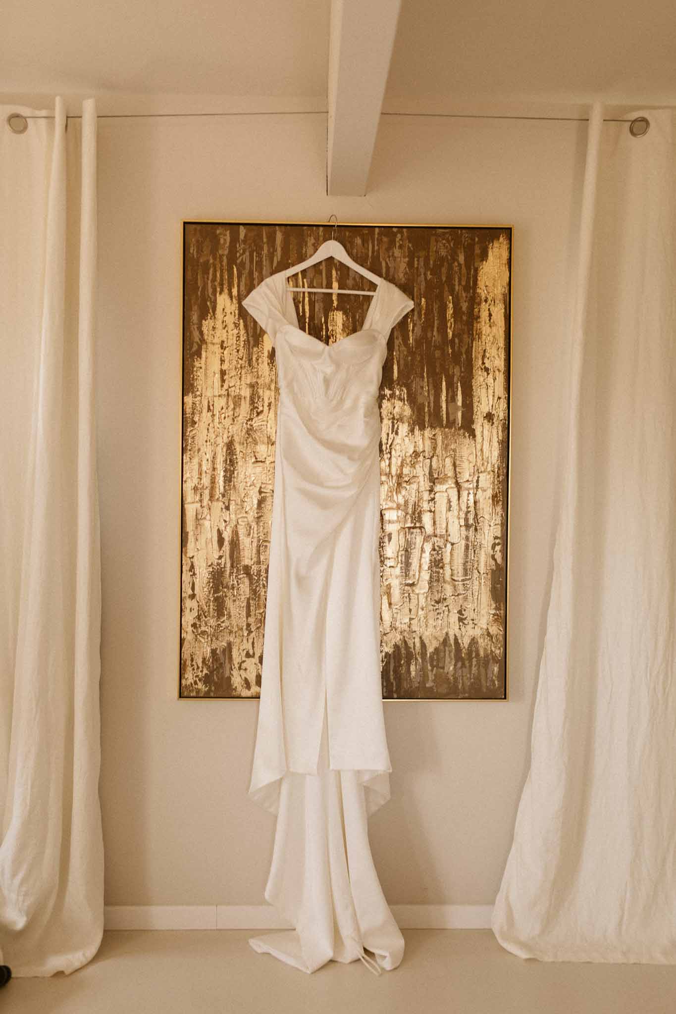 Ivory wedding dress hanging on wooden backdrop in bridal preparation room