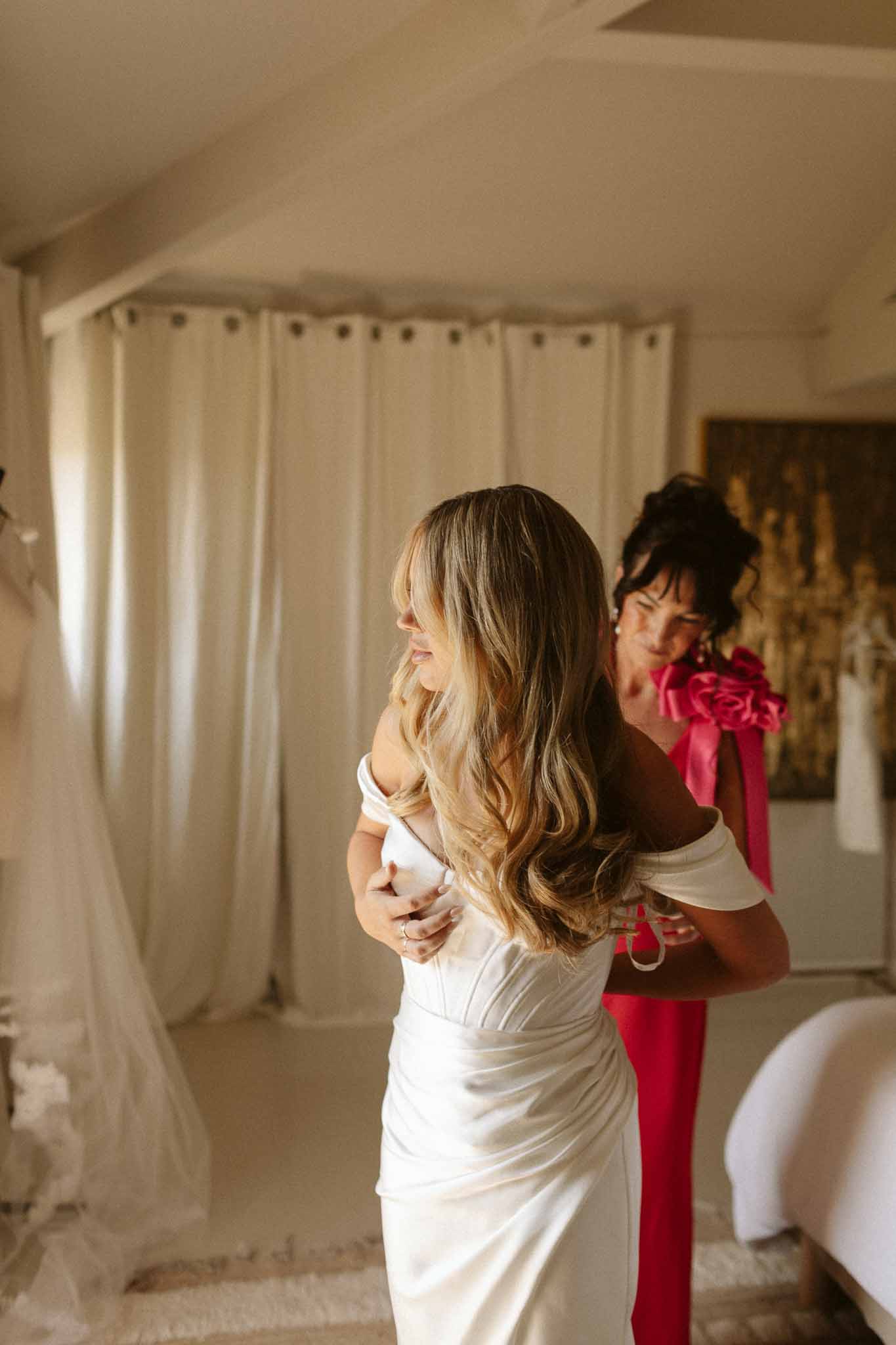 Bride in ivory dress being embraced by attendant during getting ready preparations in bridal suite