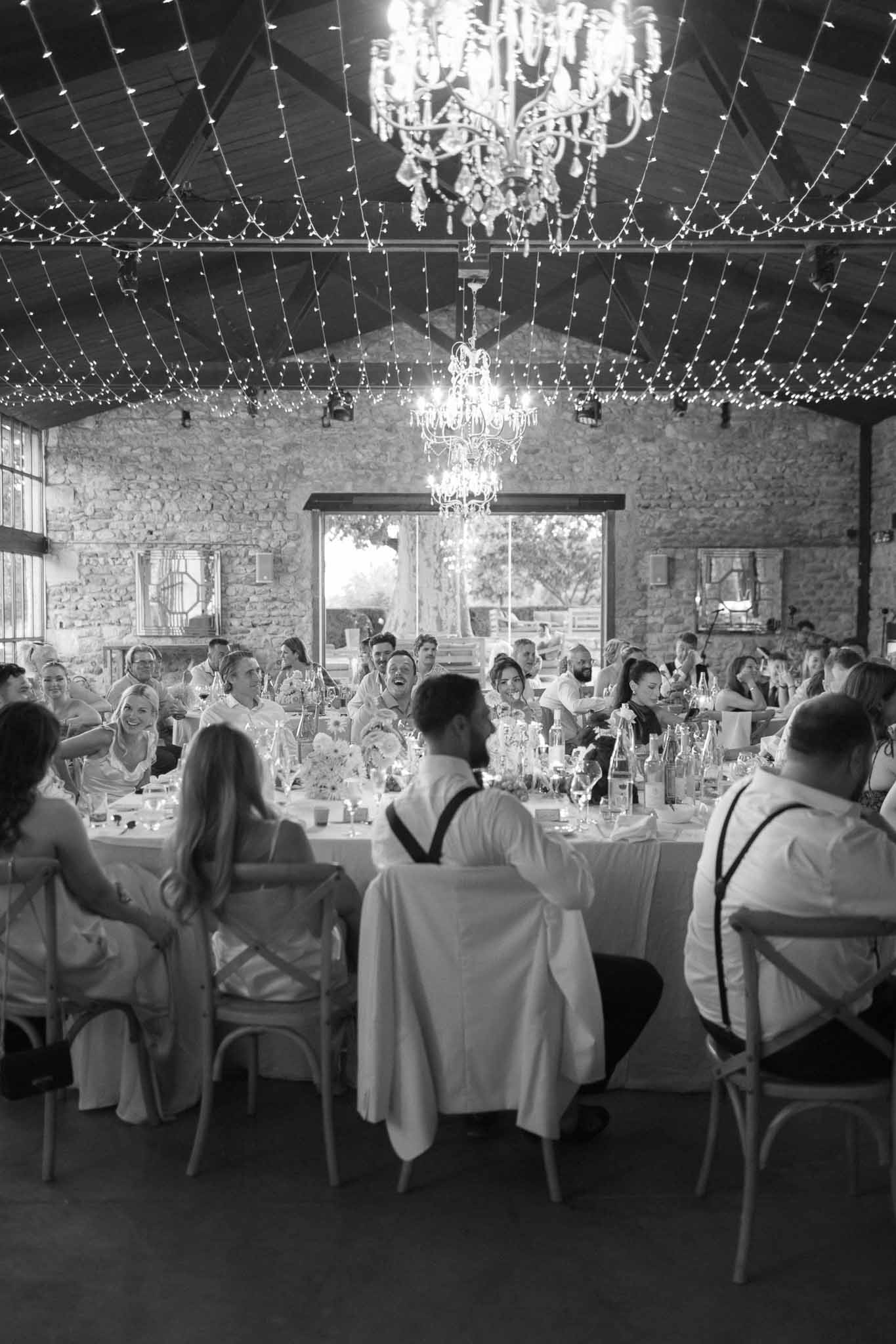 Reception dinner with guests at long tables in stone barn with geometric lighting installation overhead