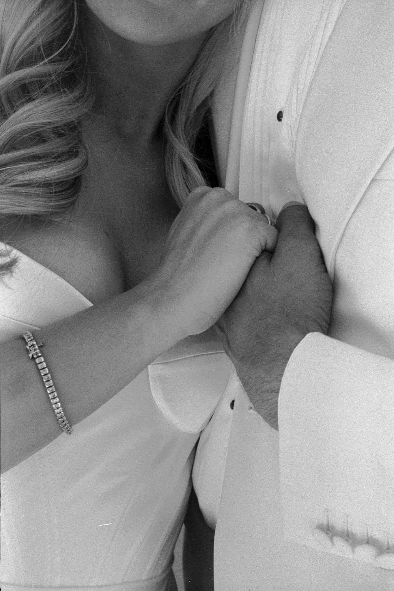 Black and white close-up of bride and groom's intertwined hands and arms during wedding portraits