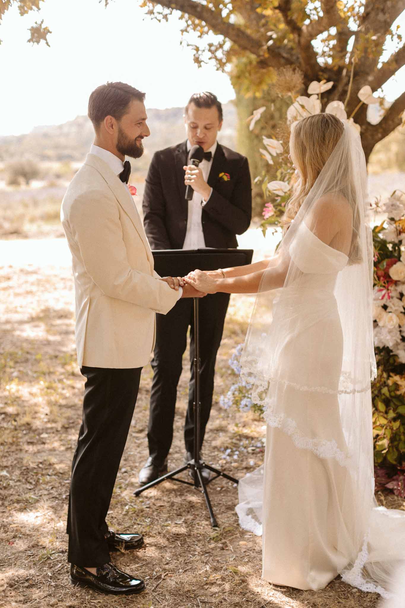 Bride and groom exchanging vows under olive tree at outdoor Mediterranean ceremony