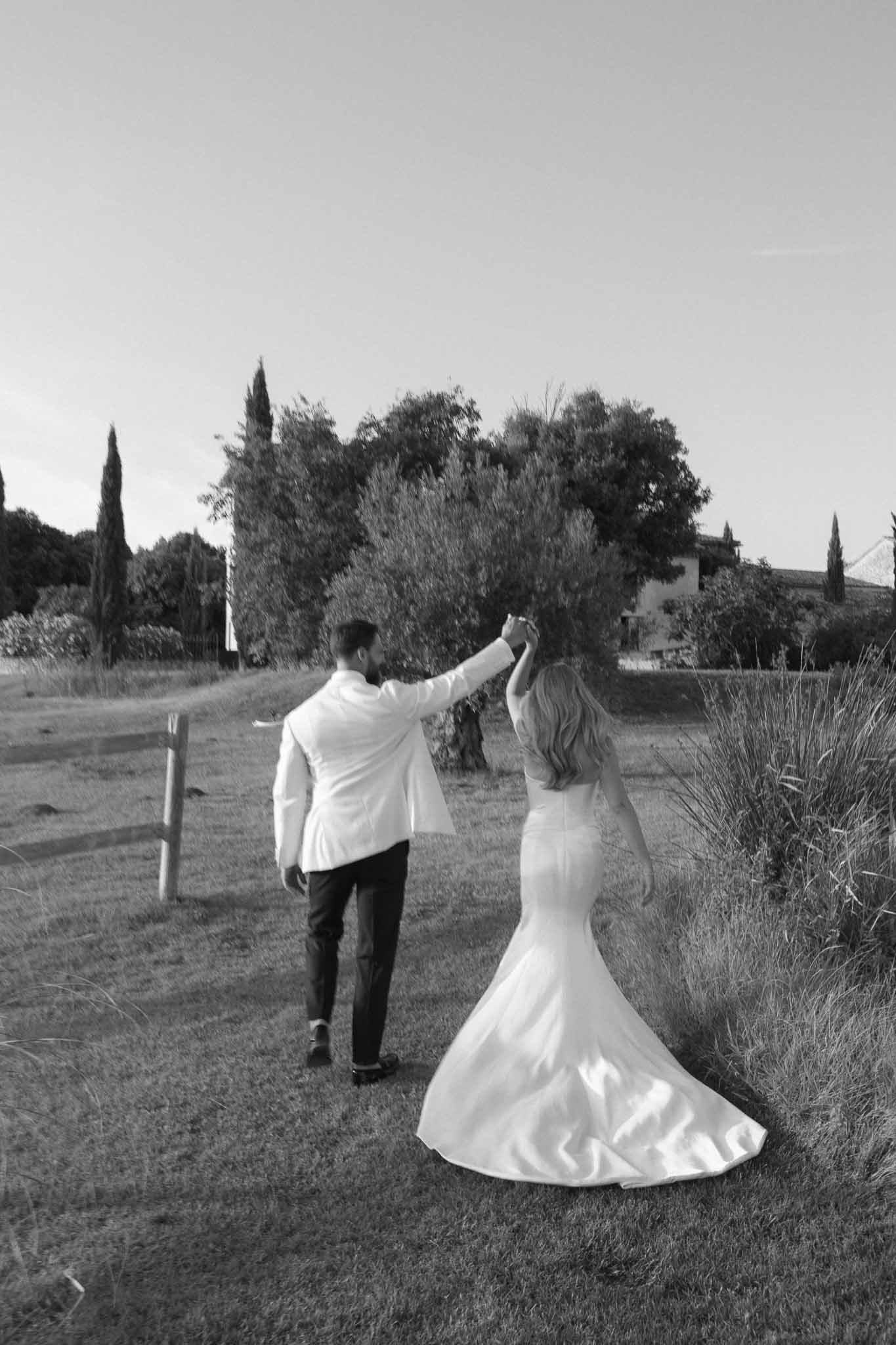 Couple walking hand in hand on countryside path with cypress trees and Mediterranean buildings