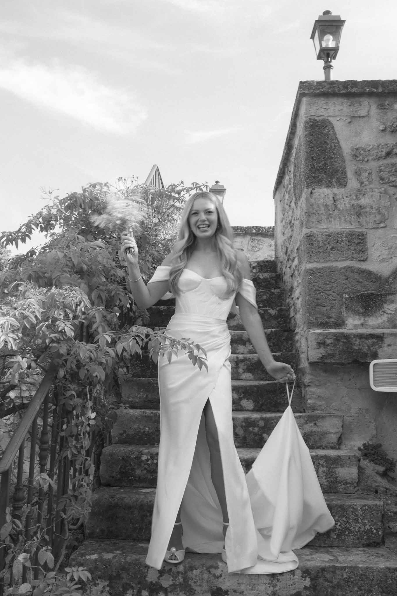 Bride in off-shoulder wedding dress on stone staircase at historic castle grounds