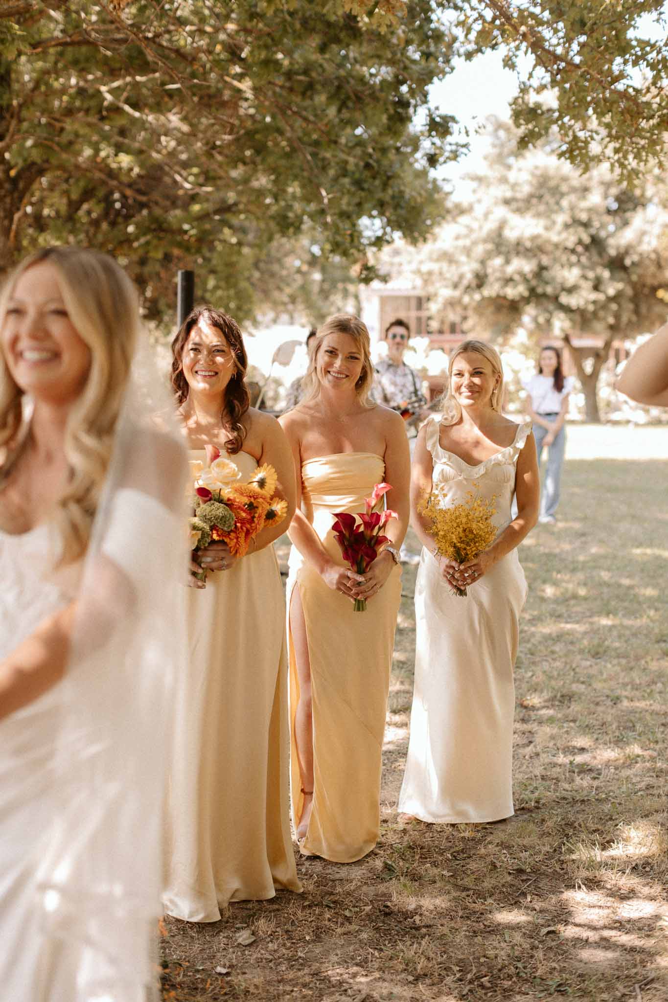Bride and bridesmaids walking in processional under trees at outdoor wedding ceremony