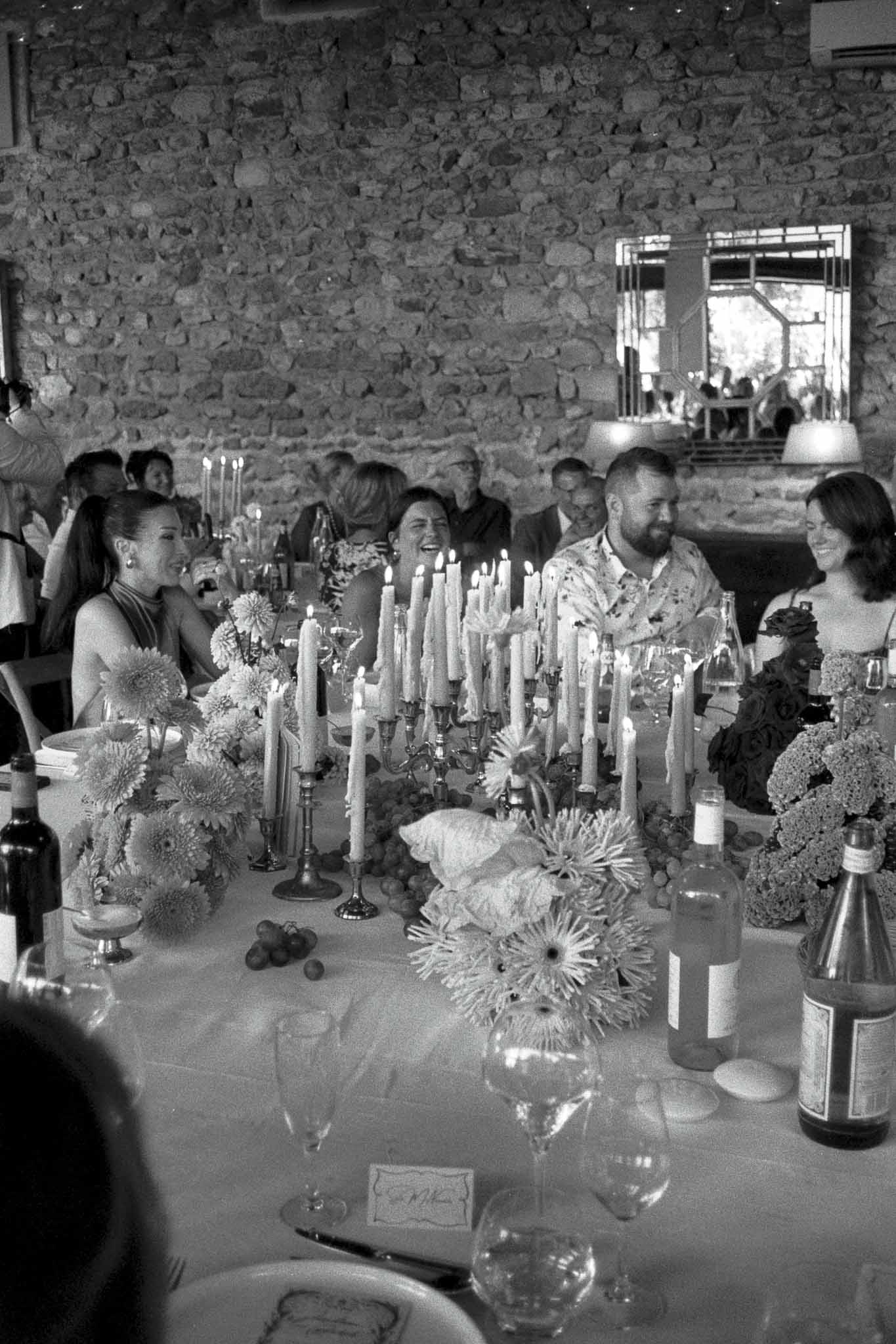 Wedding reception dinner with guests at candlelit table in indoor venue with stone walls