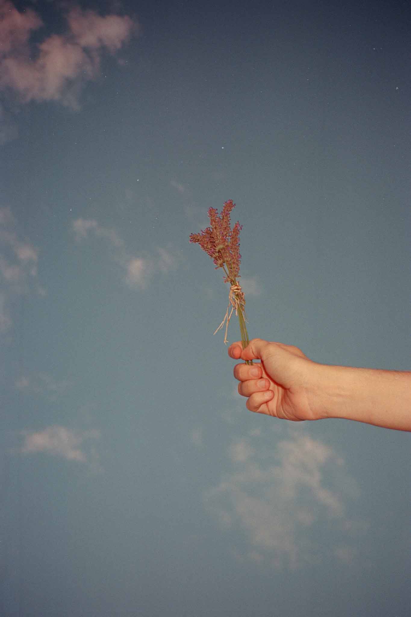 Hand holding dried terracotta flower bundle against blue sky at outdoor wedding