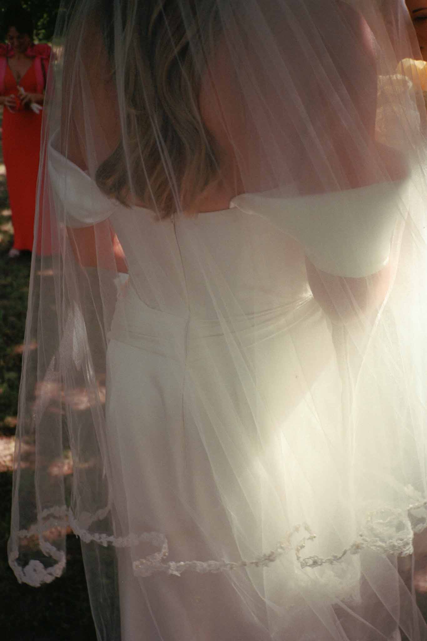 Close-up of bride's ivory silk gown and lace veil during outdoor wedding ceremony