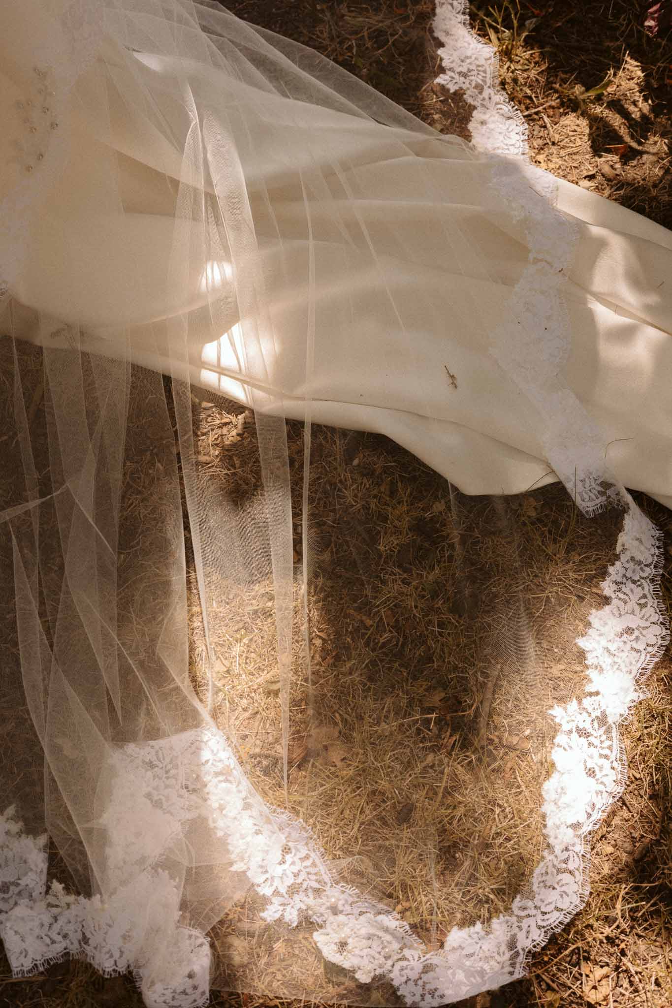 Ivory wedding dress and veil with lace trim laid on hay outdoors at rustic countryside venue