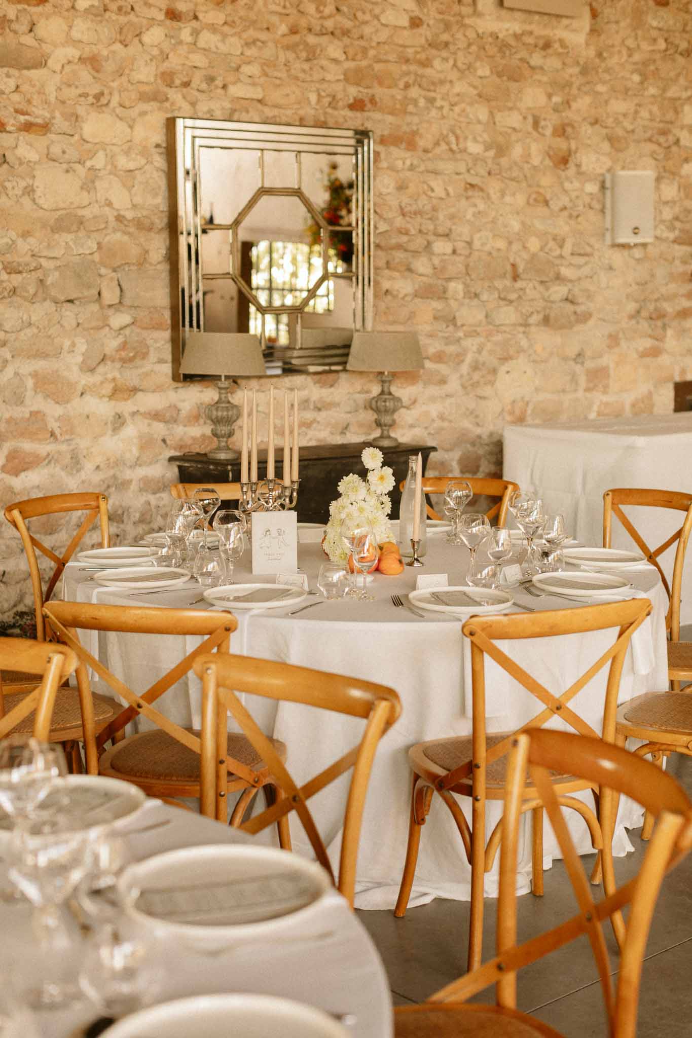 Formal dining room with round tables set for wedding reception featuring stone walls and wooden chairs