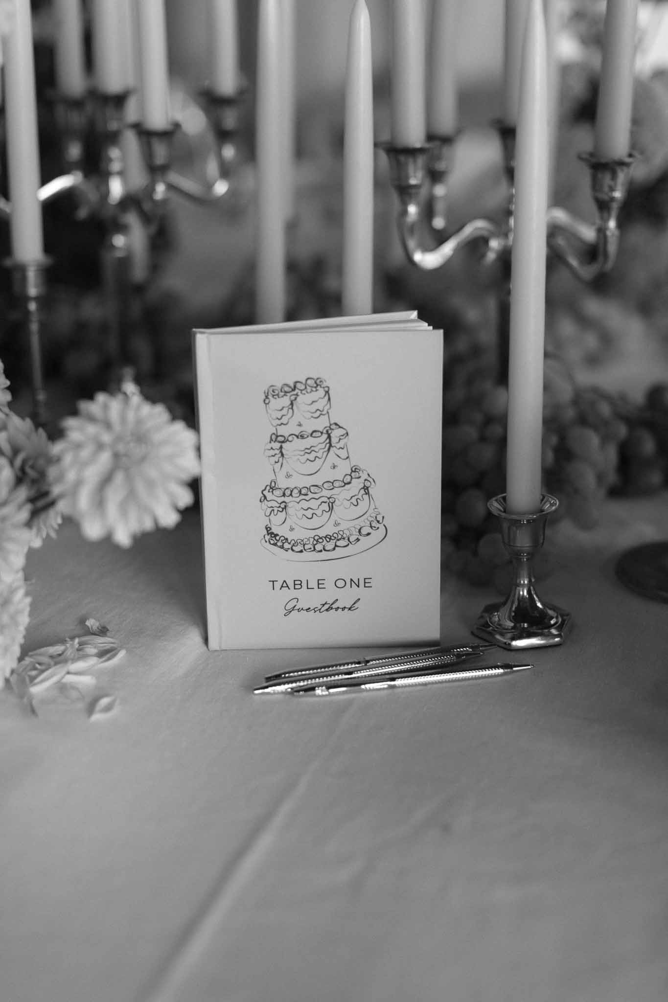 Black and white close-up of wedding reception table card and guestbook setup with candles