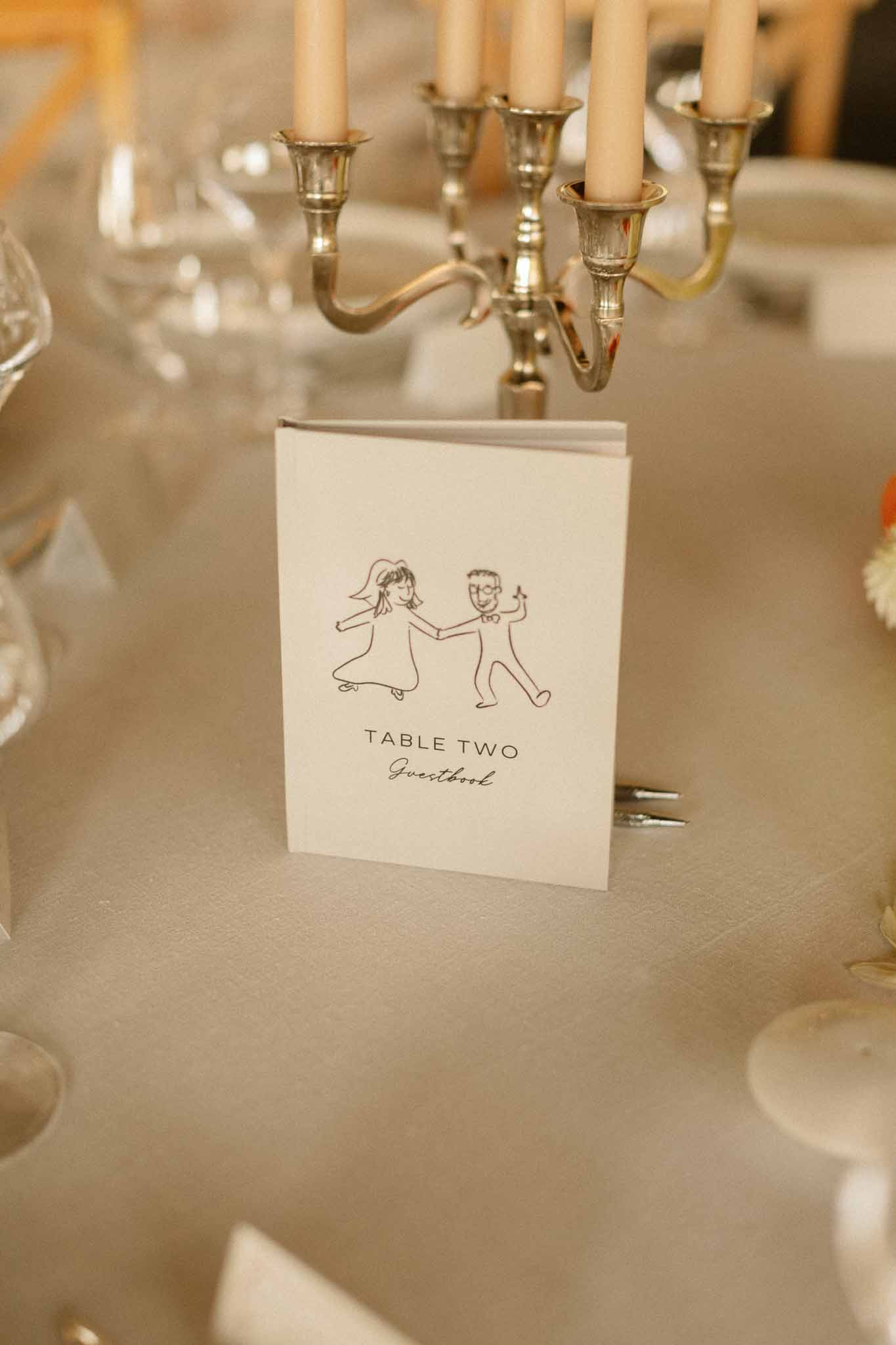 Table number card with bride and groom illustration and brass candelabra at wedding reception