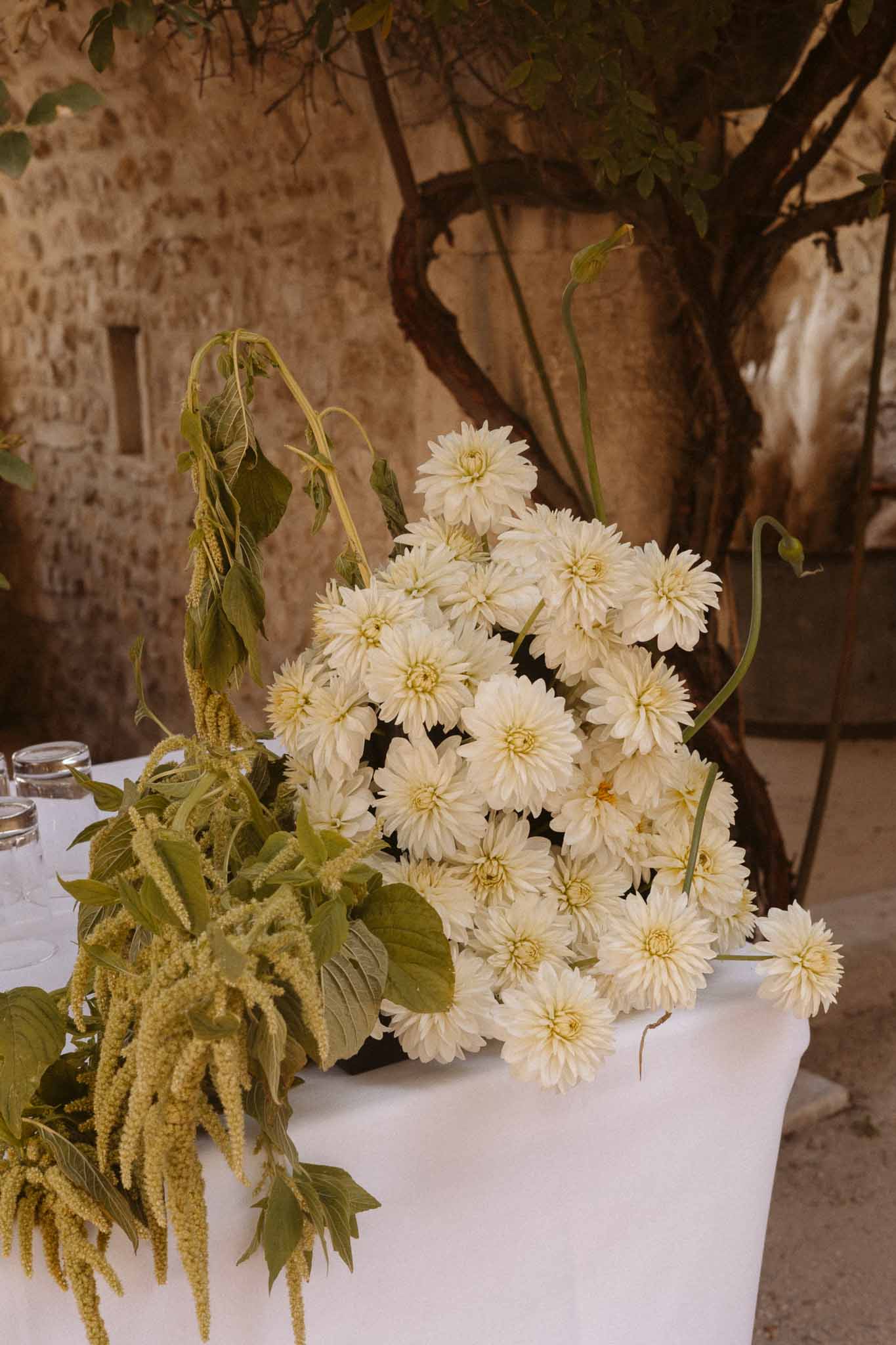 Close-up floral arrangement with cream dahlias and chartreuse amaranthus on white table in stone courtyard