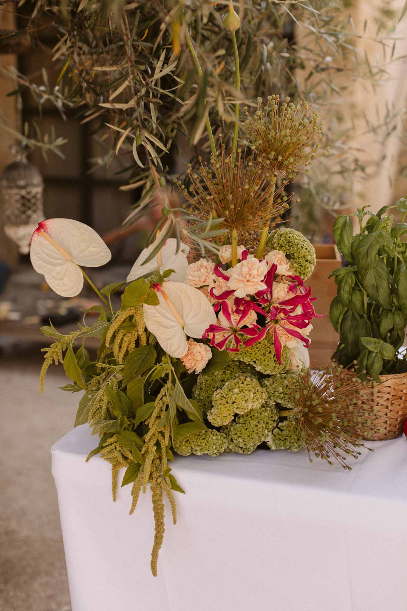 Wedding floral arrangement with anthurium and burgundy astilbe on white-draped table at reception venue