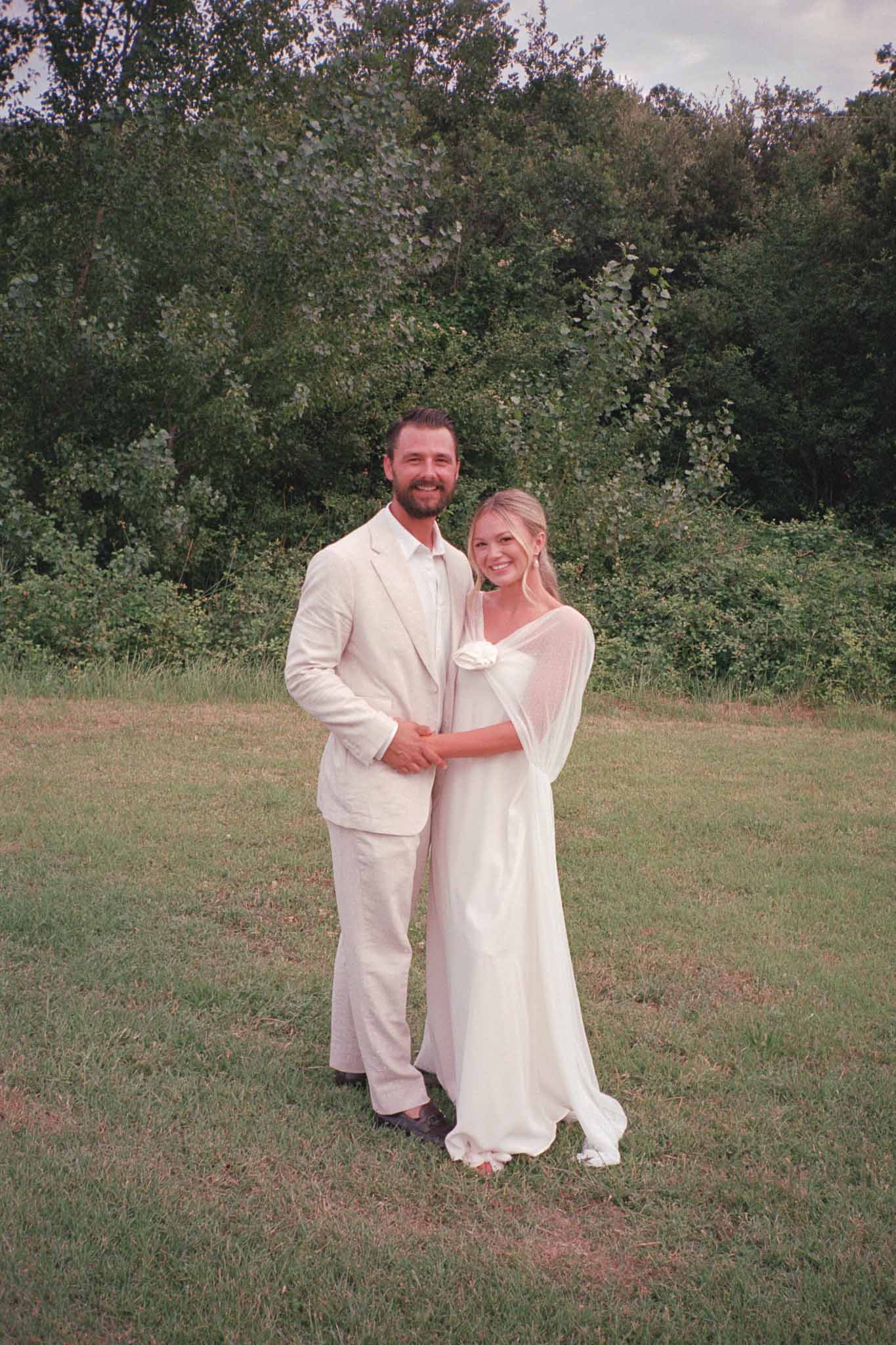 Couple in cream and ivory formal attire posing in outdoor garden setting