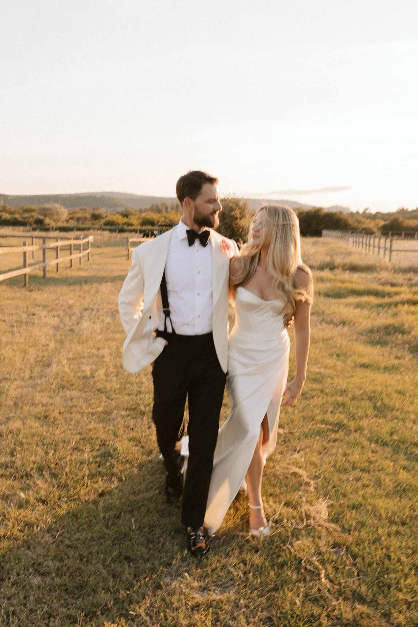 Bride and groom walking together through pastoral landscape during golden hour at rural wedding venue