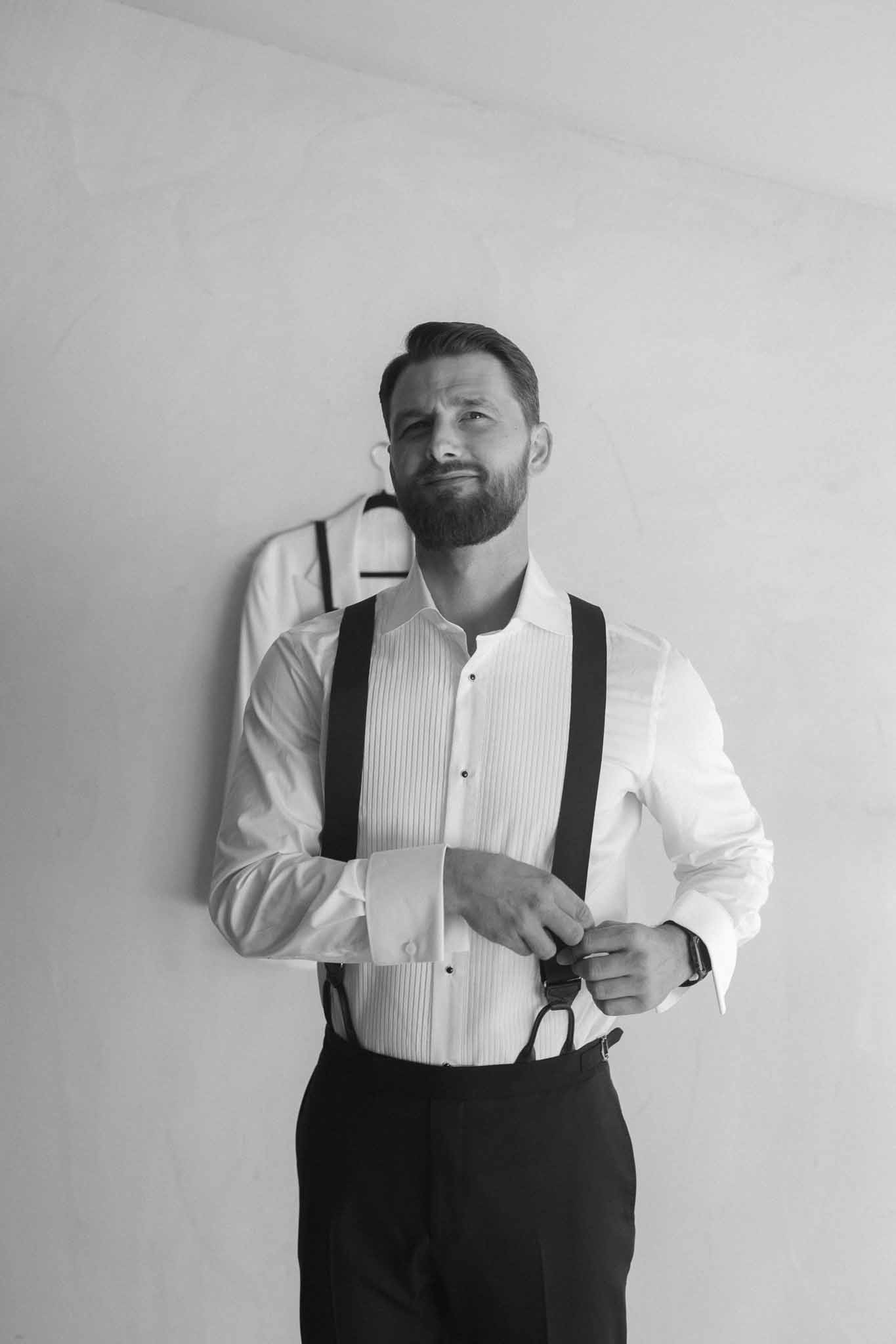 Black and white groom portrait adjusting bow tie in wedding attire at studio