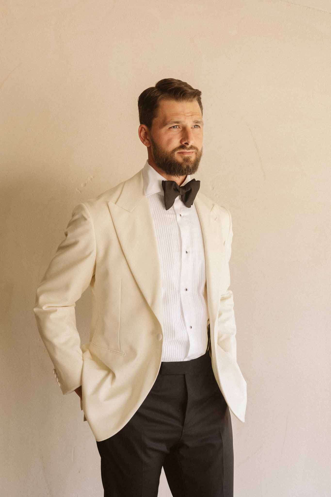 Groom in cream jacket and black bow tie formal portrait against neutral background