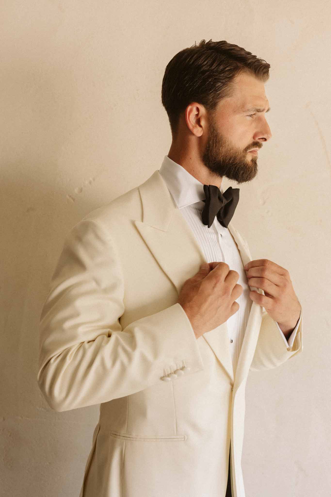 Groom in cream tuxedo adjusting jacket during formal portrait session