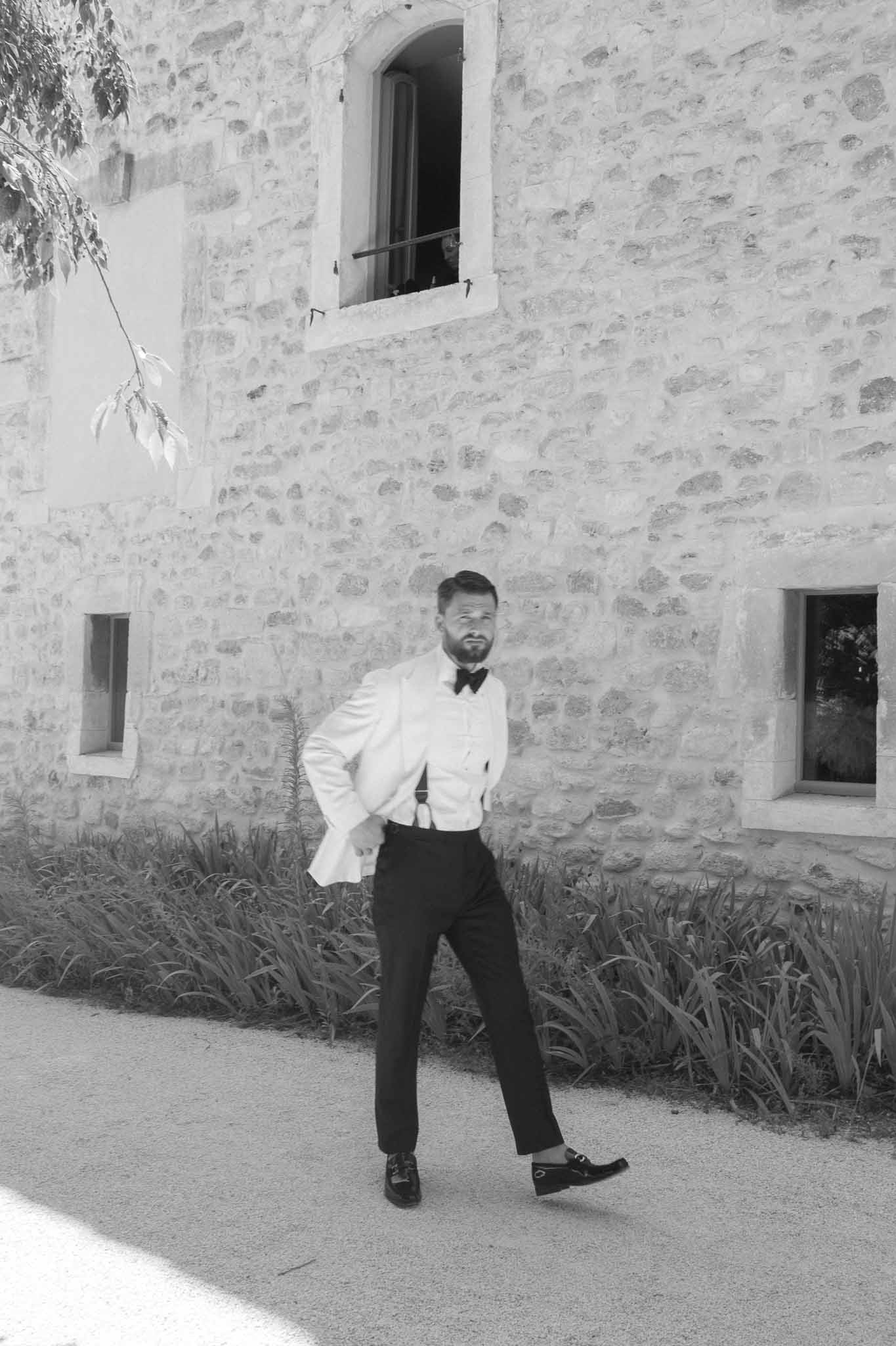 Groom in black bow tie posing against historic stone building exterior