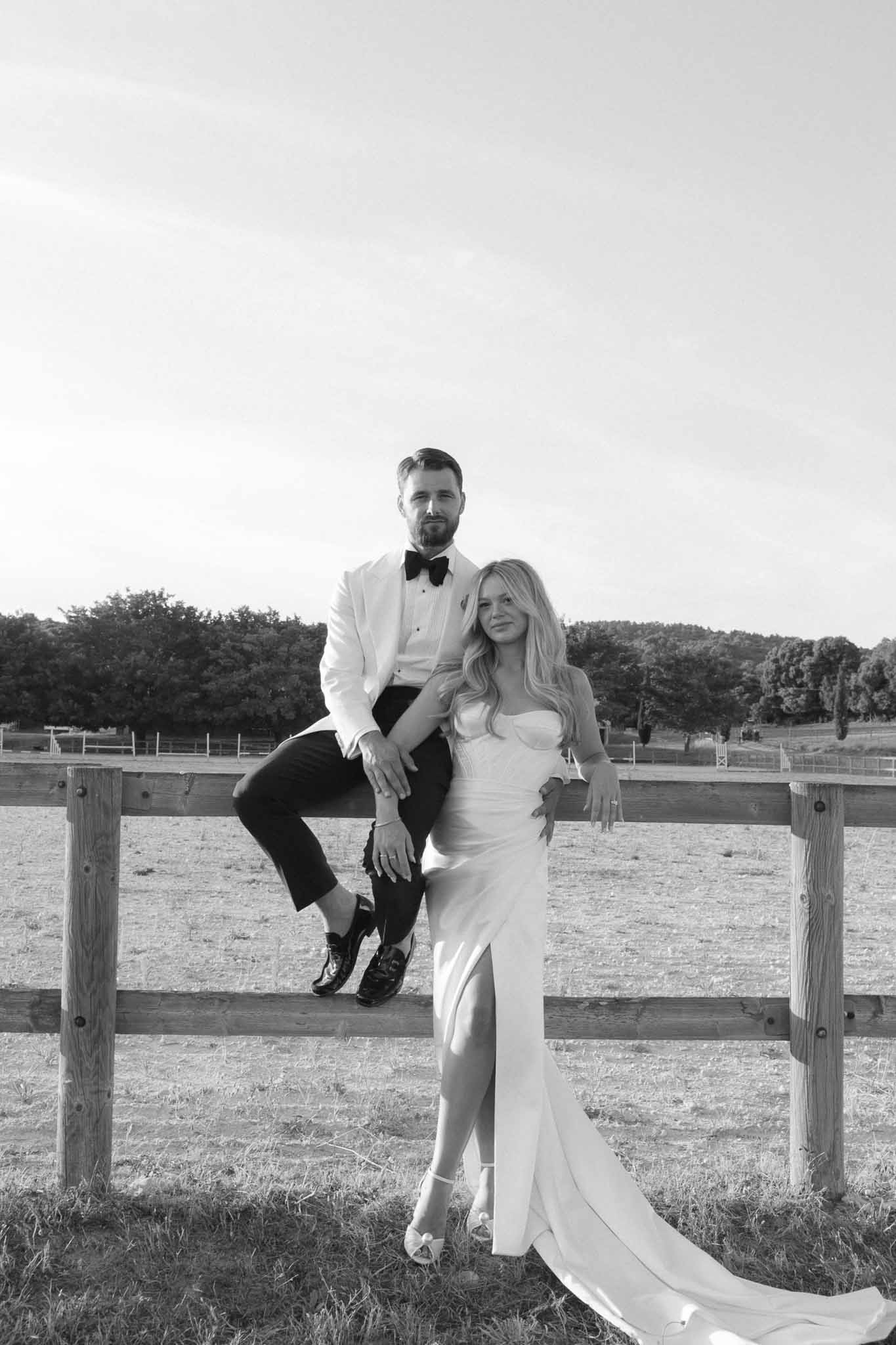 Bride and groom posing together on wooden fence at rural ranch property