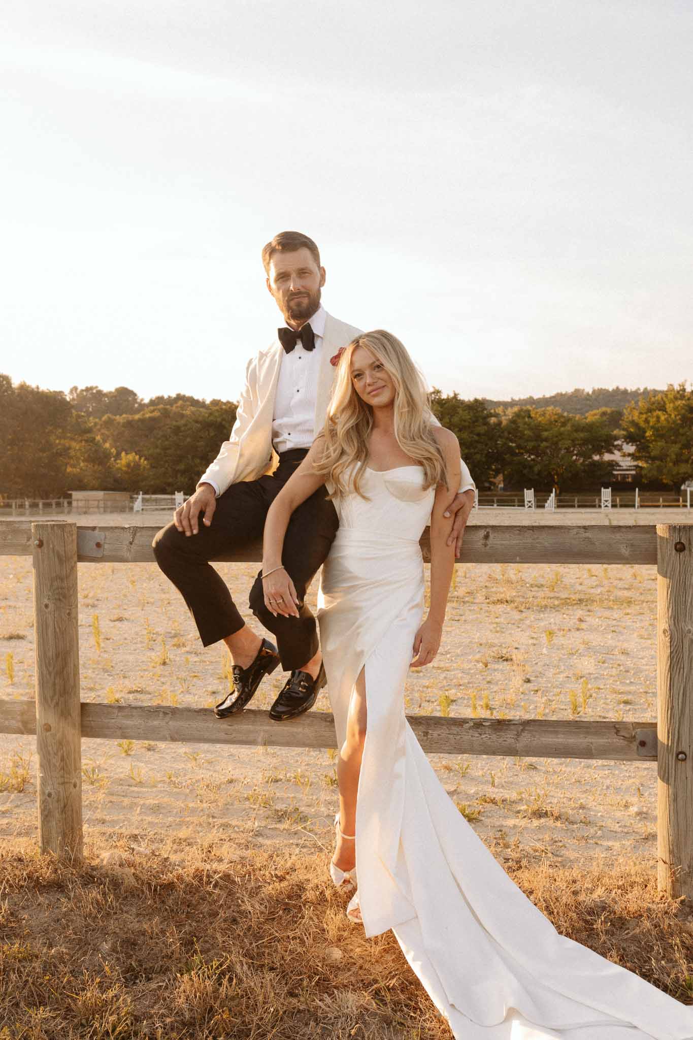 Bride and groom portrait at outdoor equestrian venue with wooden fence and countryside backdrop