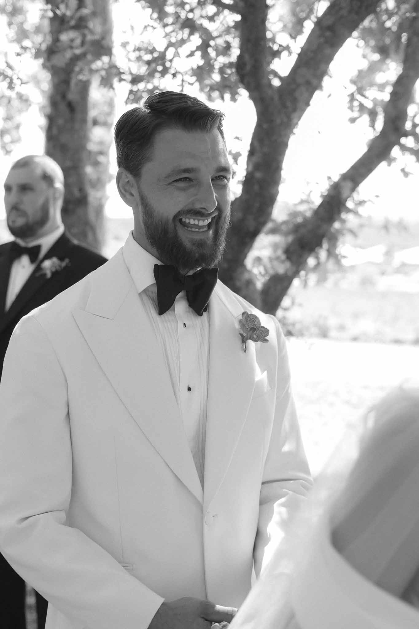 Groom smiling during outdoor wedding ceremony under mature trees