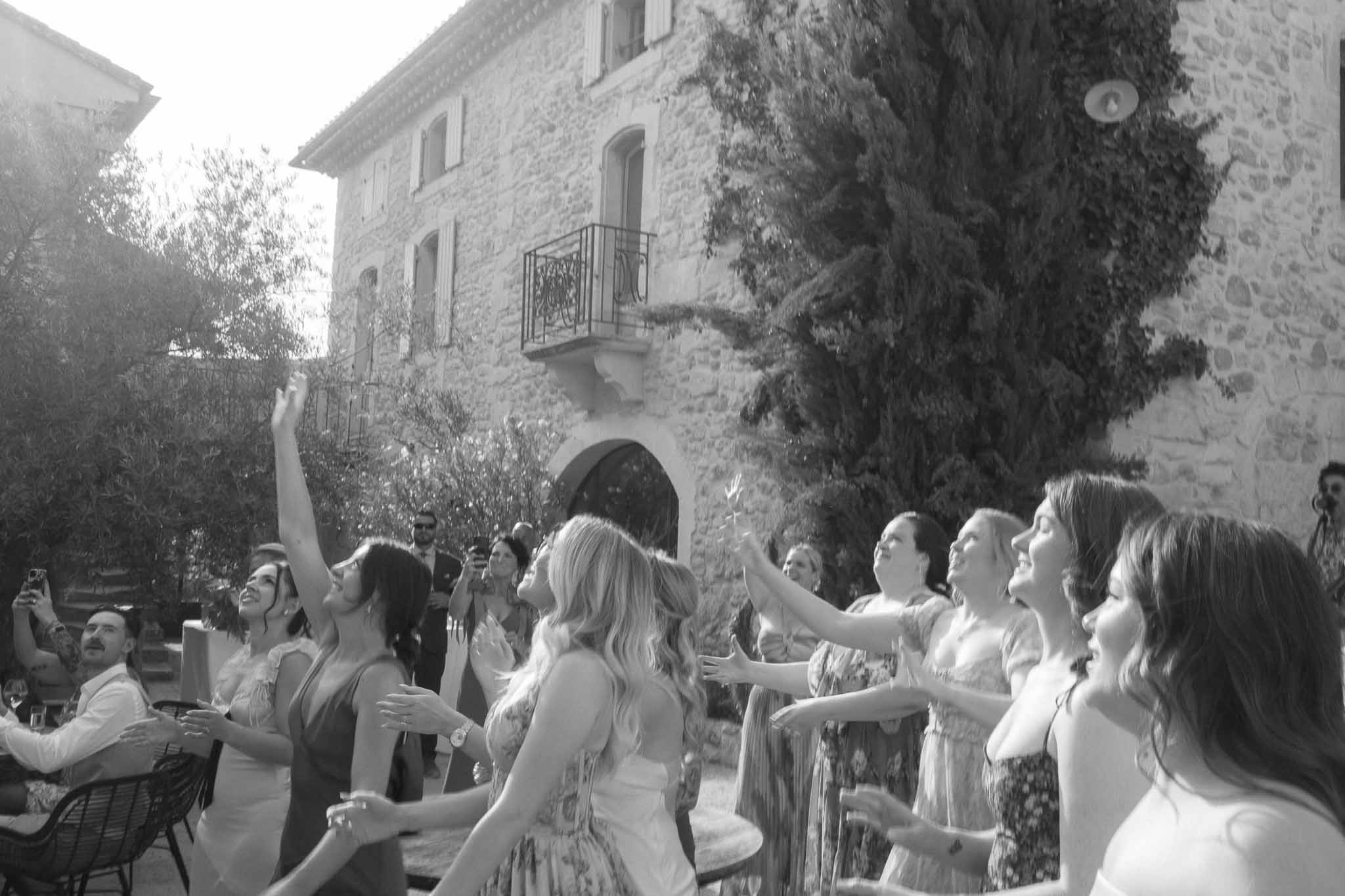 Wedding guests watching bouquet toss in historic stone courtyard during reception celebration