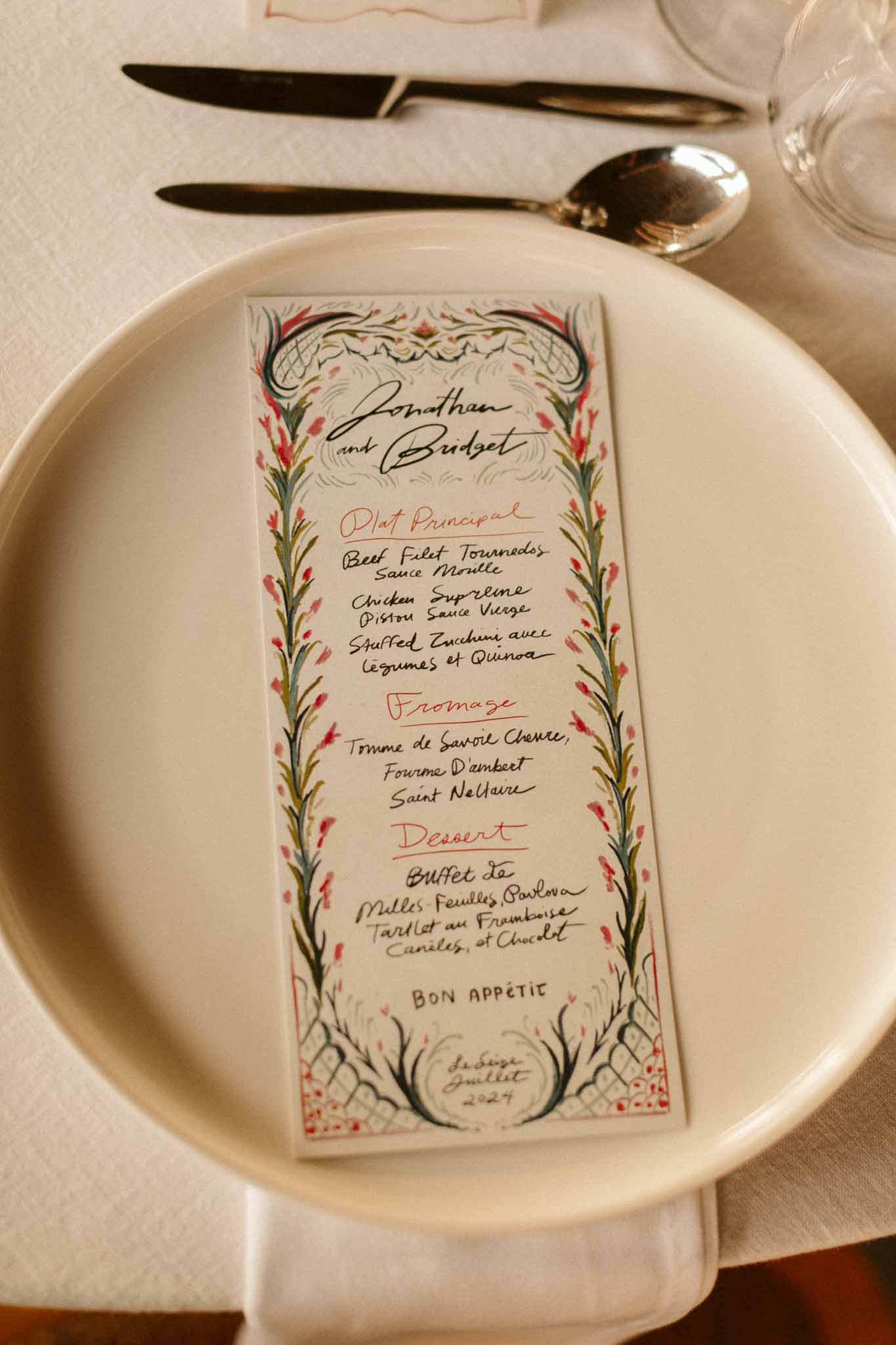 Handwritten menu card with botanical details on cream plate at wedding reception table setting