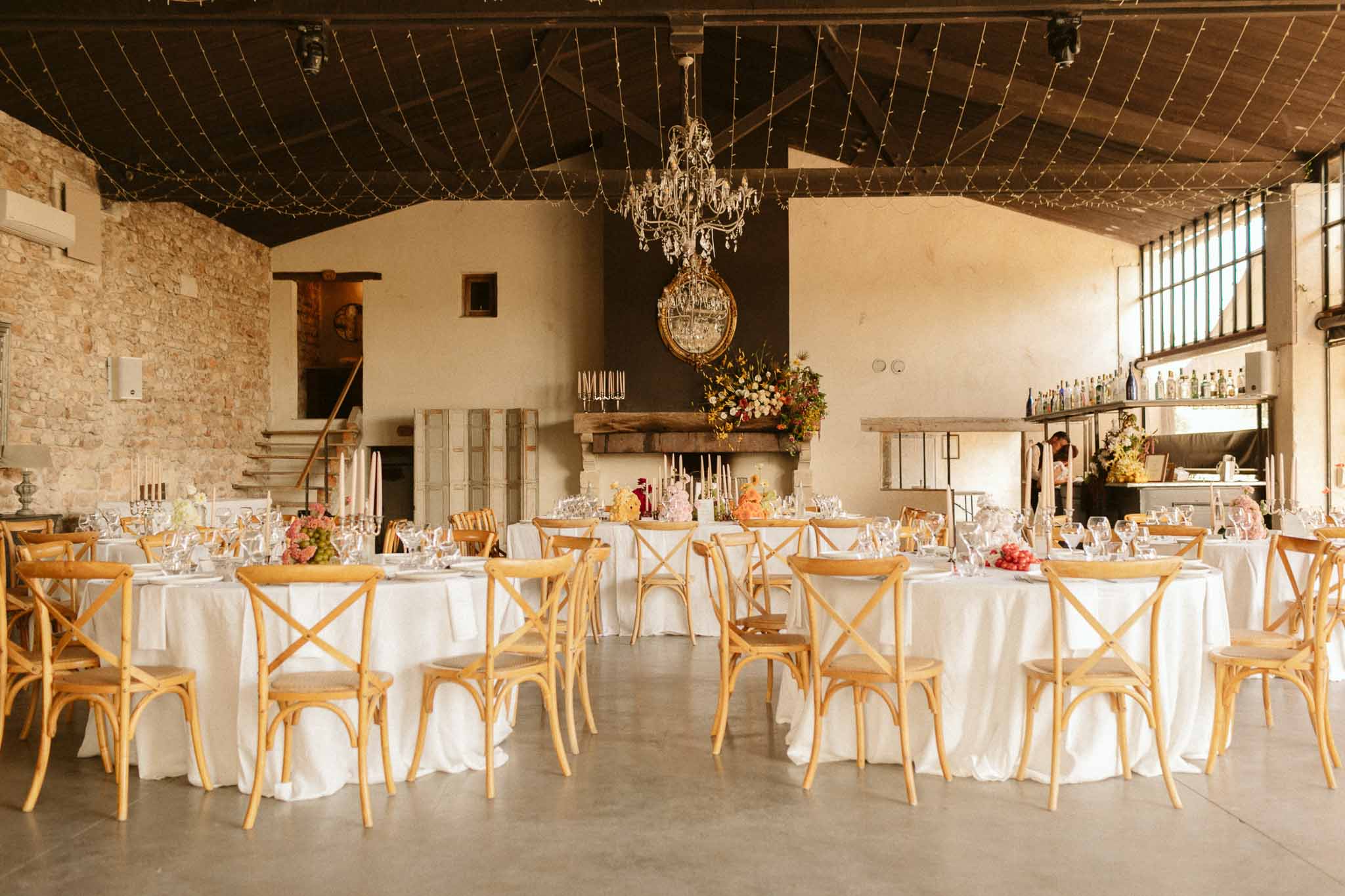 Wedding reception with round tables and fairy lights in industrial venue with exposed stone walls