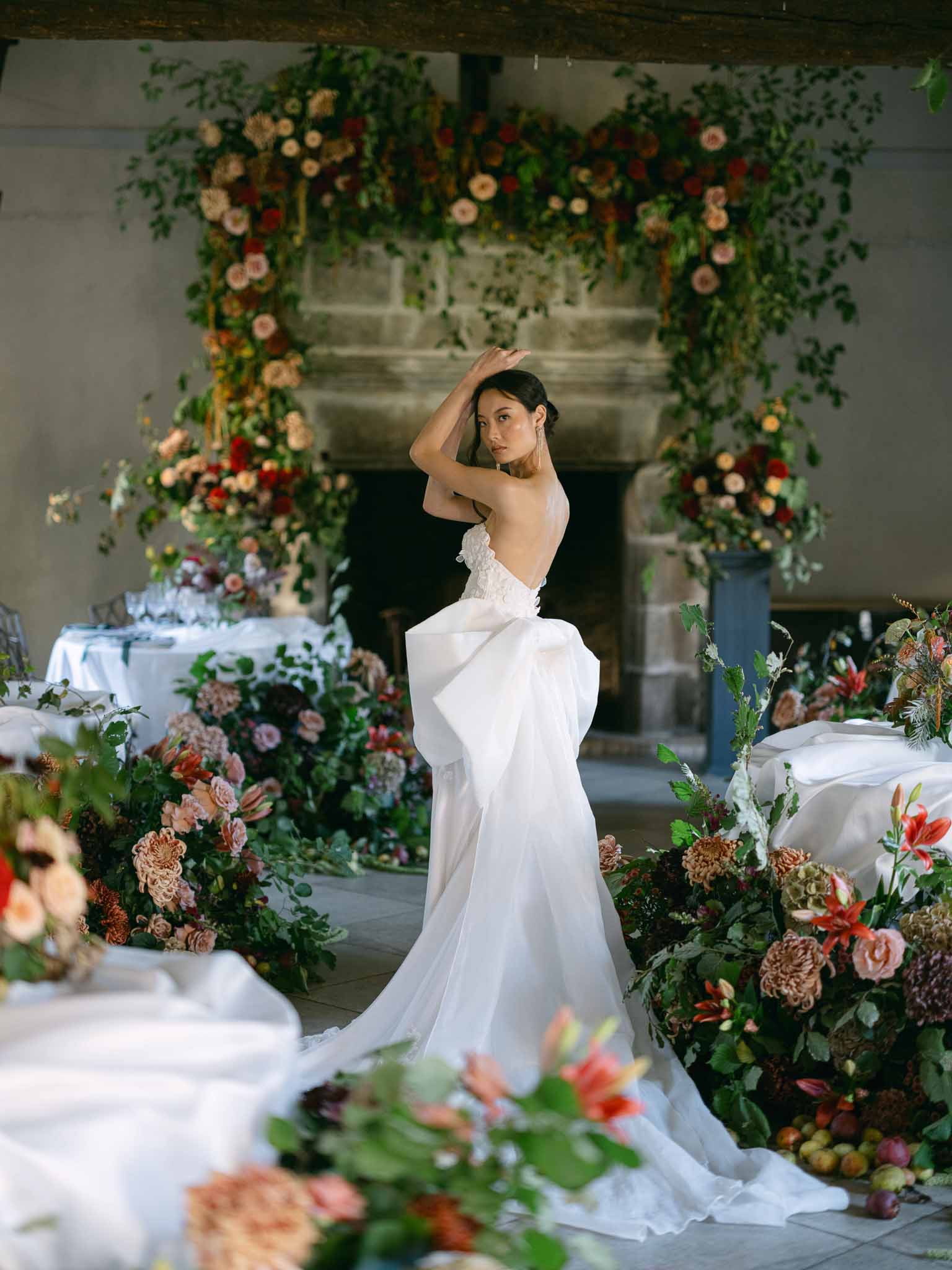 Bride in ivory strapless gown poses among elaborate floral installations in indoor reception space