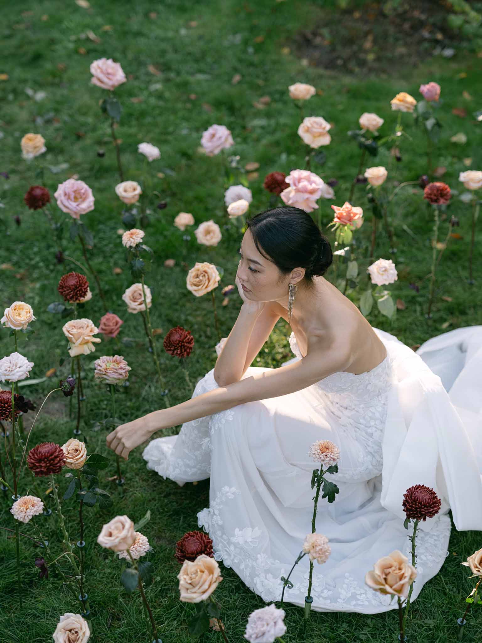 Bride in ivory lace dress sitting among roses in romantic garden portrait session