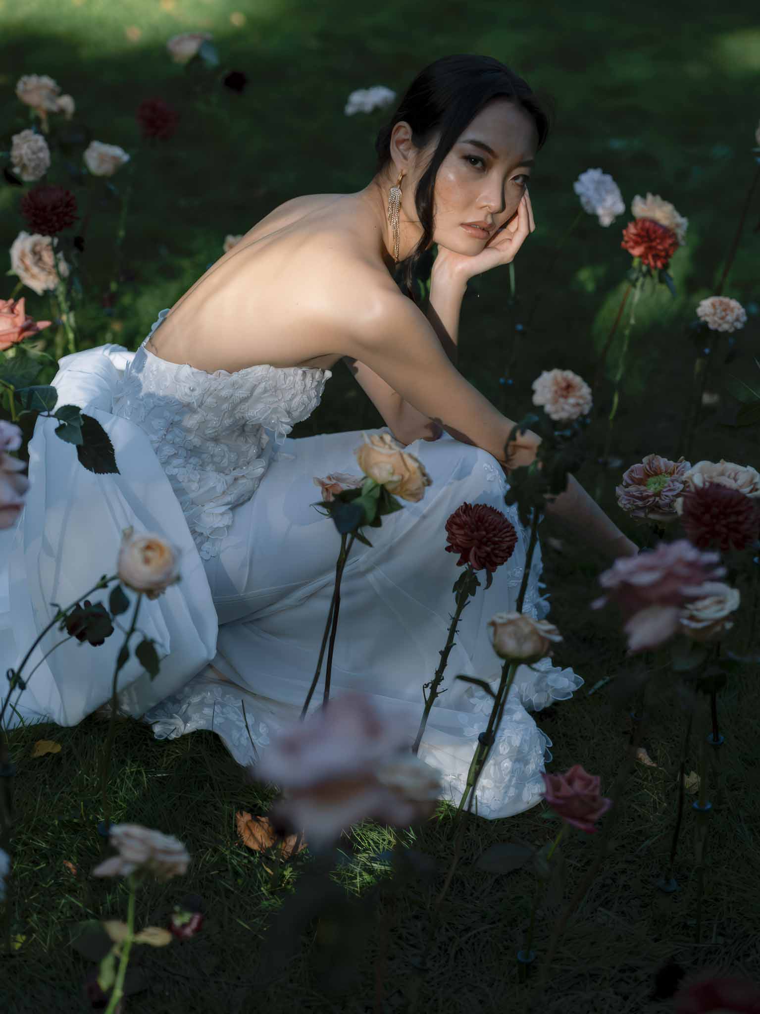 Bride in white lace dress posing among dahlia and rose garden flowers