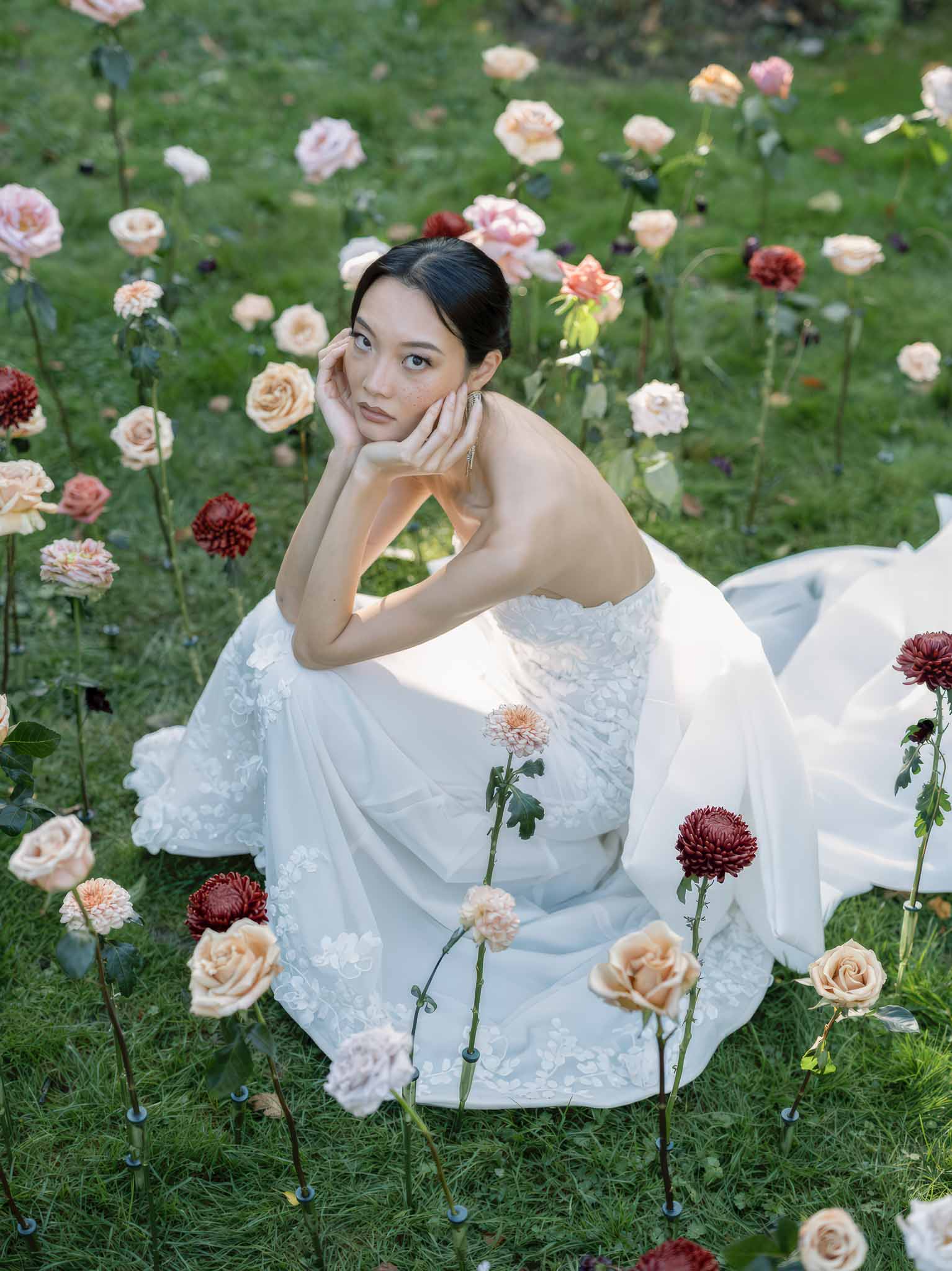 Bride in ivory lace dress sitting among dahlia and rose garden in portrait style photograph
