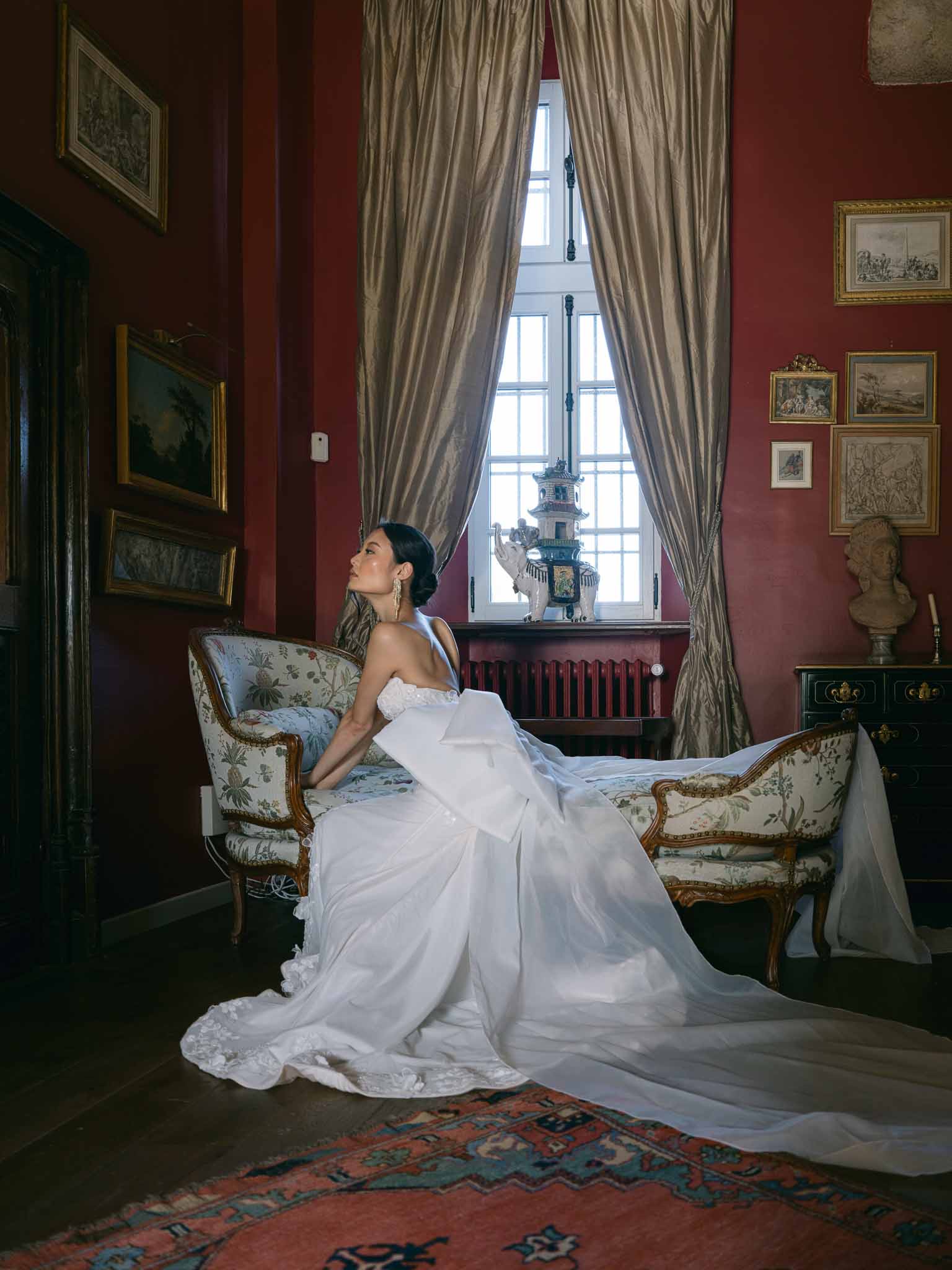 Bride in ivory gown seated in classical interior with burgundy walls and ornate furnishings