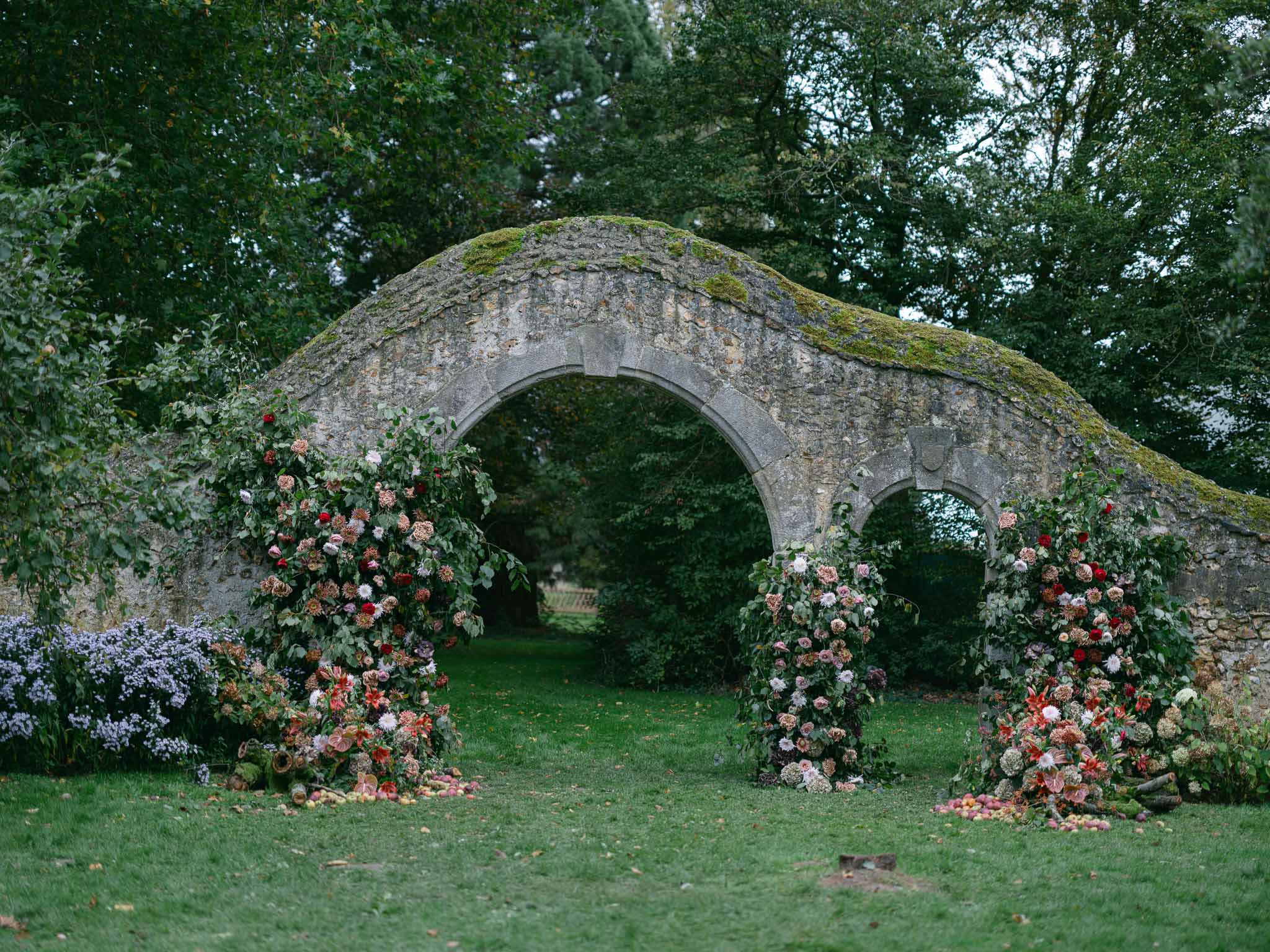 Stone bridge ceremony backdrop with floral arrangements at garden wedding venue