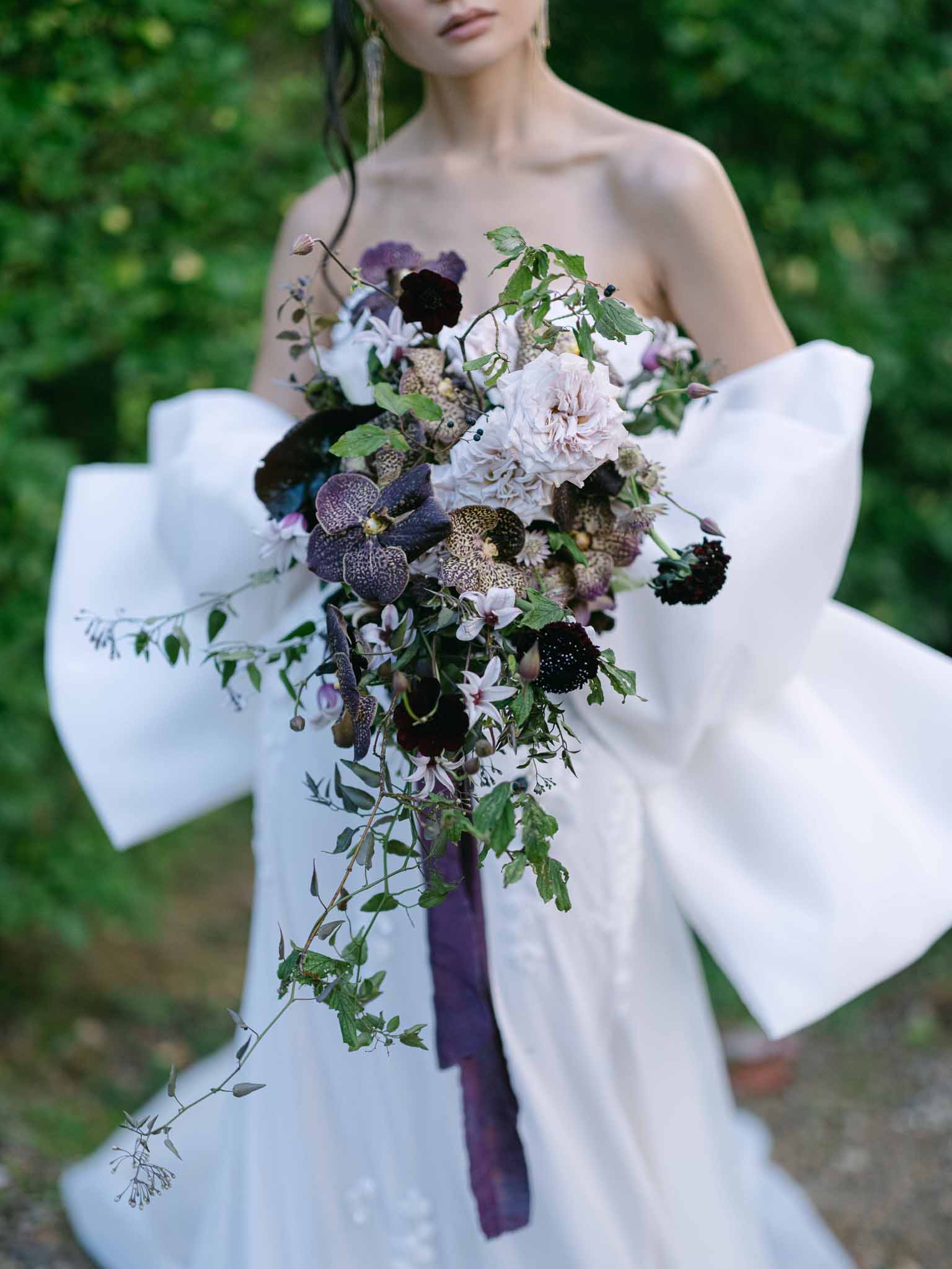 Bride holding burgundy dahlia bouquet in white strapless gown at garden wedding