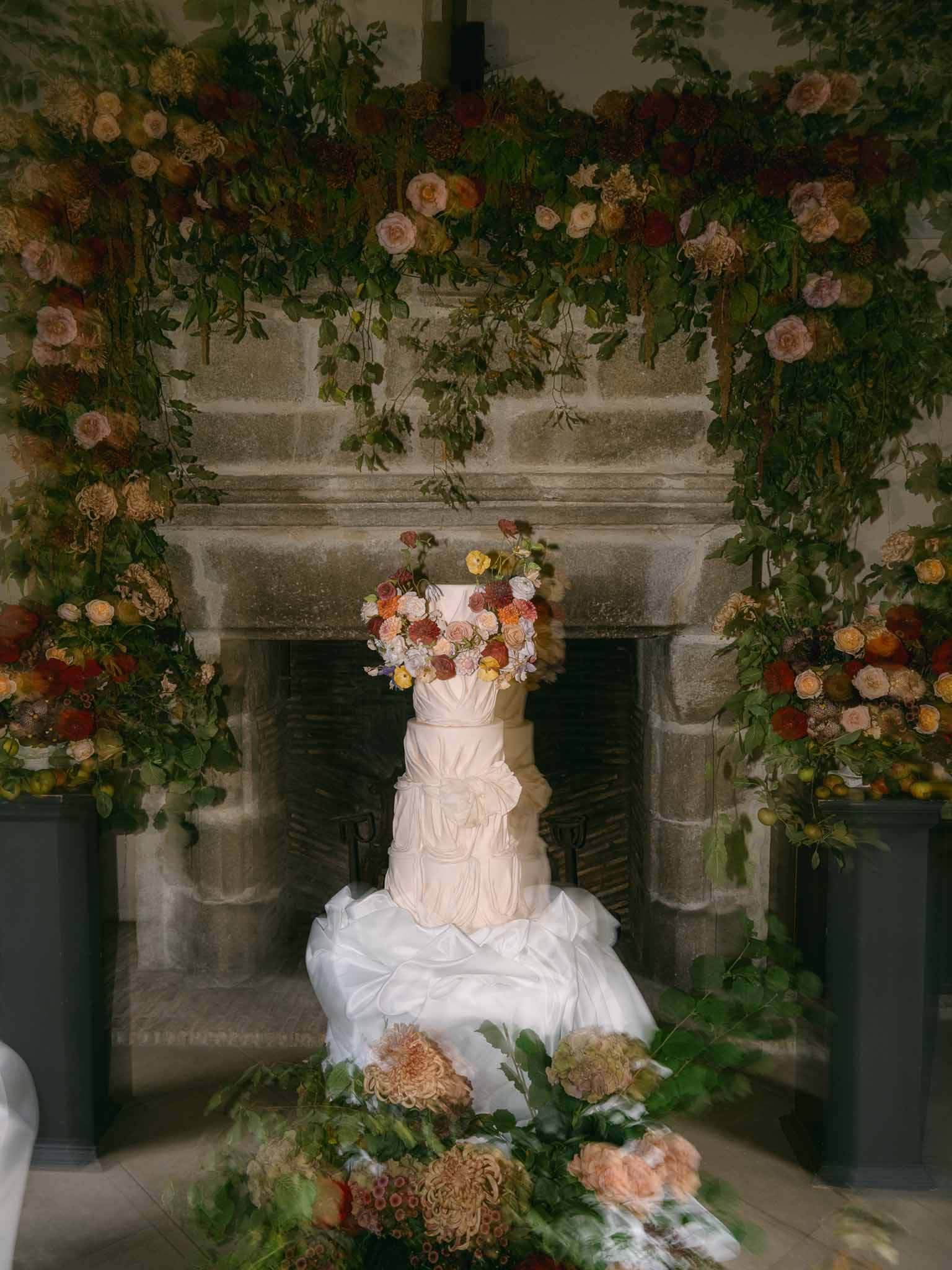 Multi-tiered wedding cake with coral and peach florals in stone alcove setting