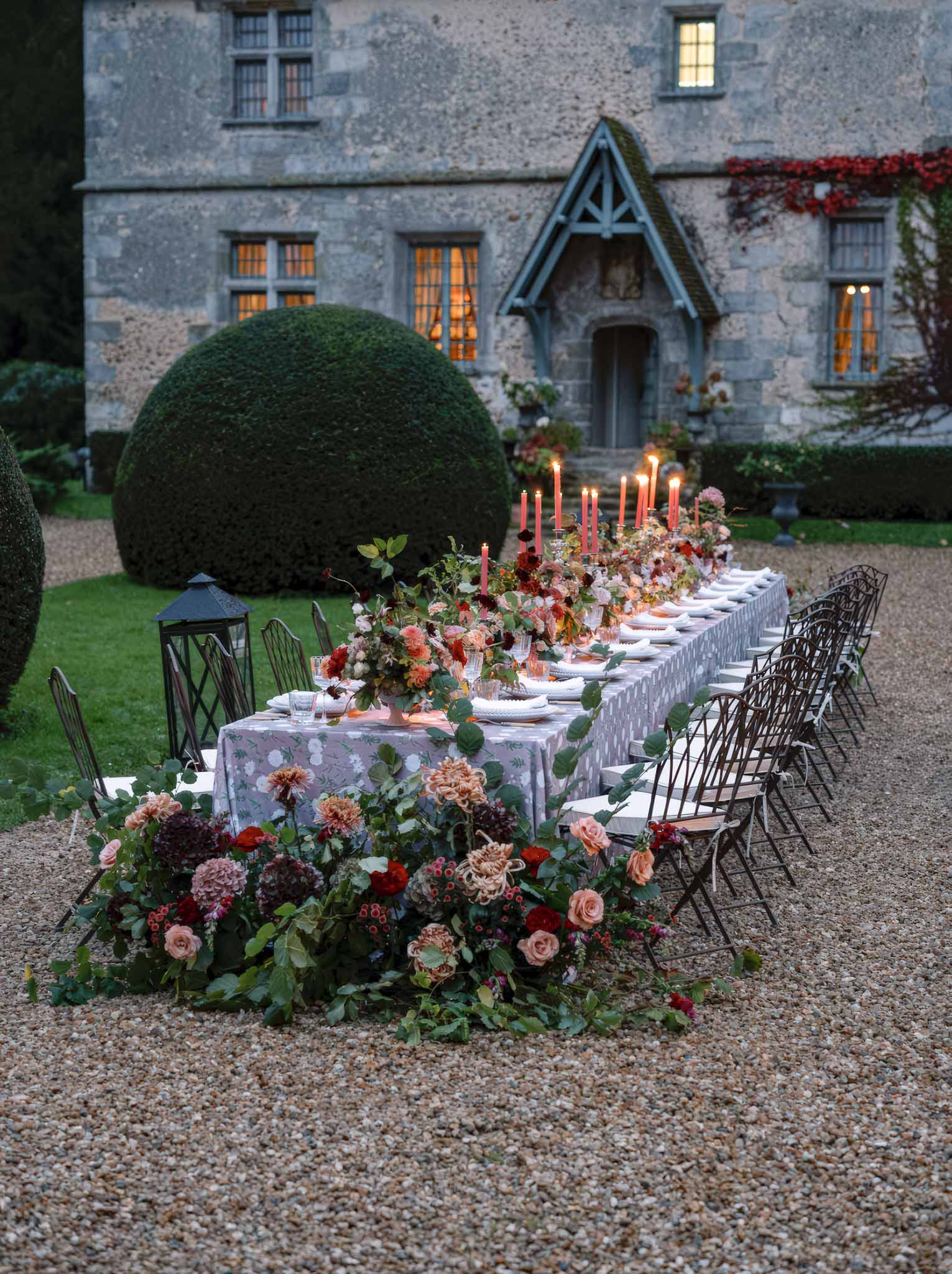 Elegant outdoor reception table setting with floral arrangements at historic stone manor house courtyard