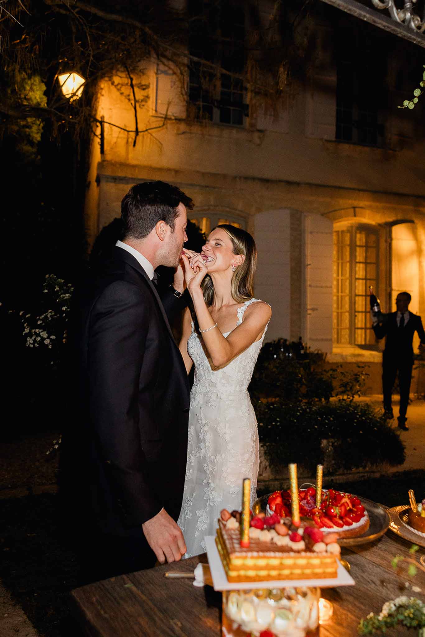 Bride and groom sharing cake during dessert service at stone courtyard evening reception