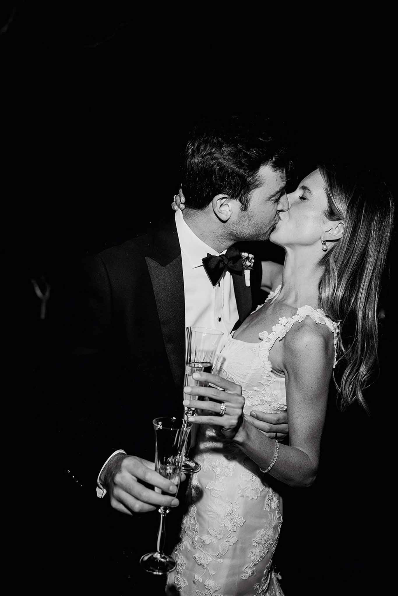 Bride and groom sharing intimate kiss with champagne flutes during wedding reception