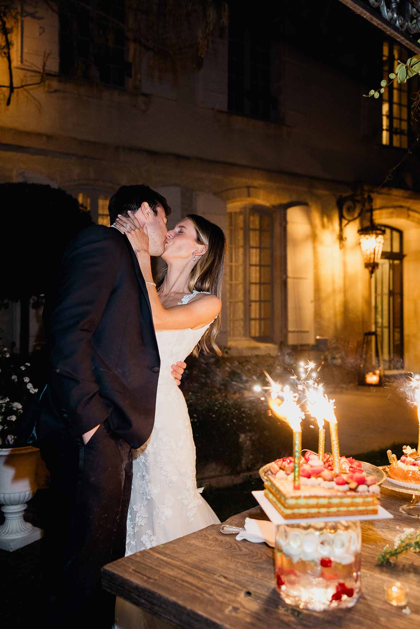 Bride and groom kissing during evening reception cake cutting at historic stone venue
