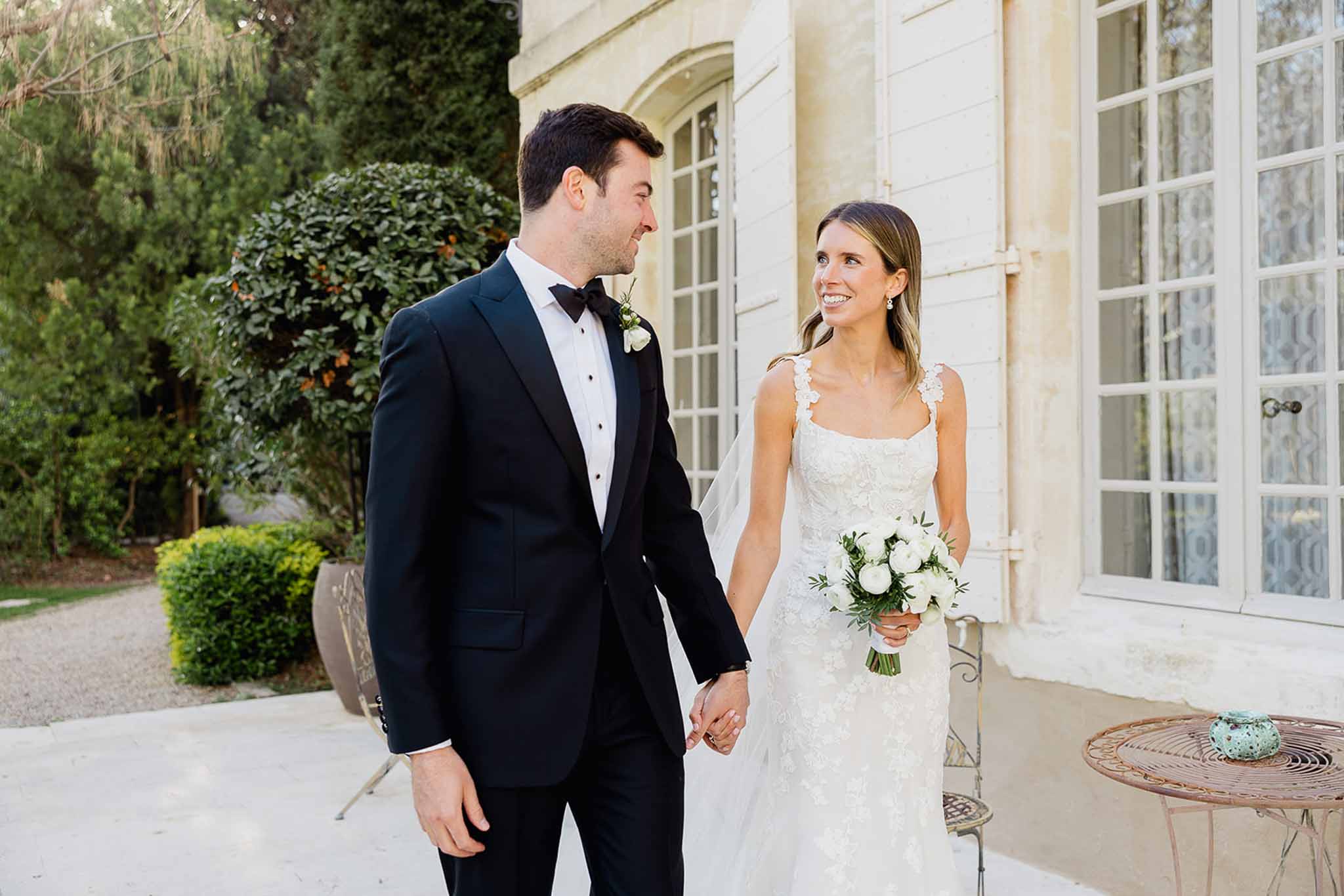 Bride and groom walking hand in hand in front of classical stone manor courtyard