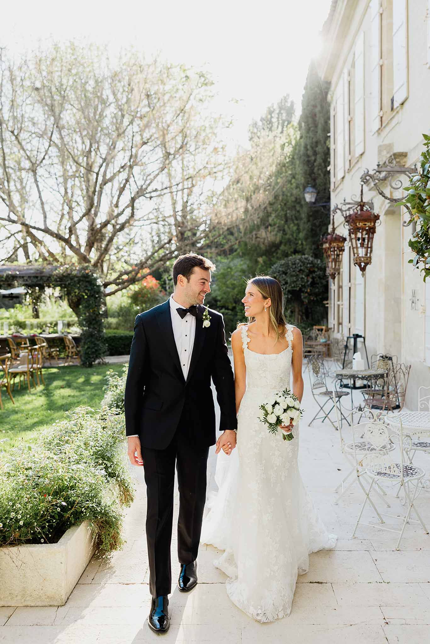 Bride and groom walking hand-in-hand on stone terrace at classical manor house during portrait session
