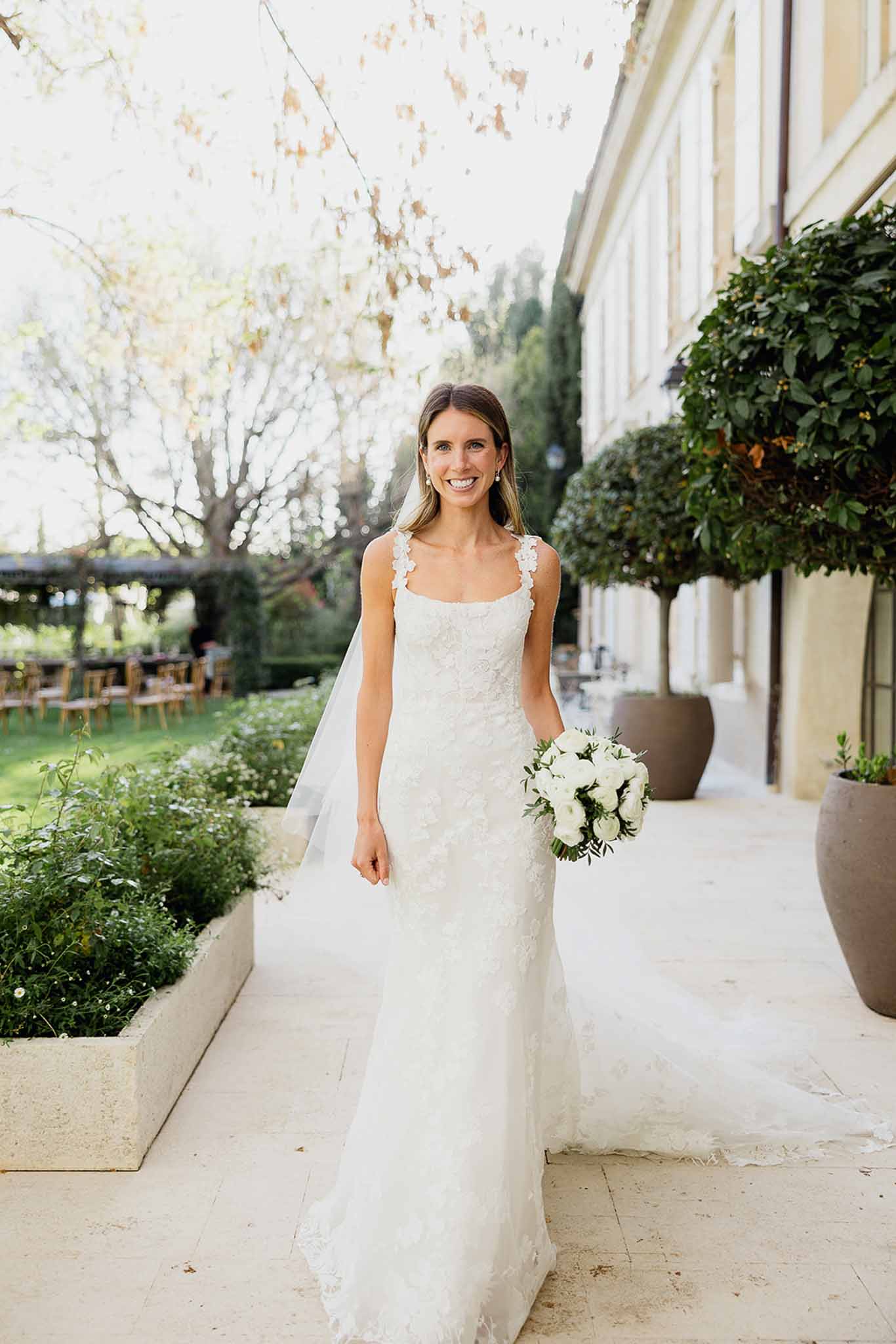 Bride in ivory lace mermaid gown standing on stone terrace at courtyard garden venue
