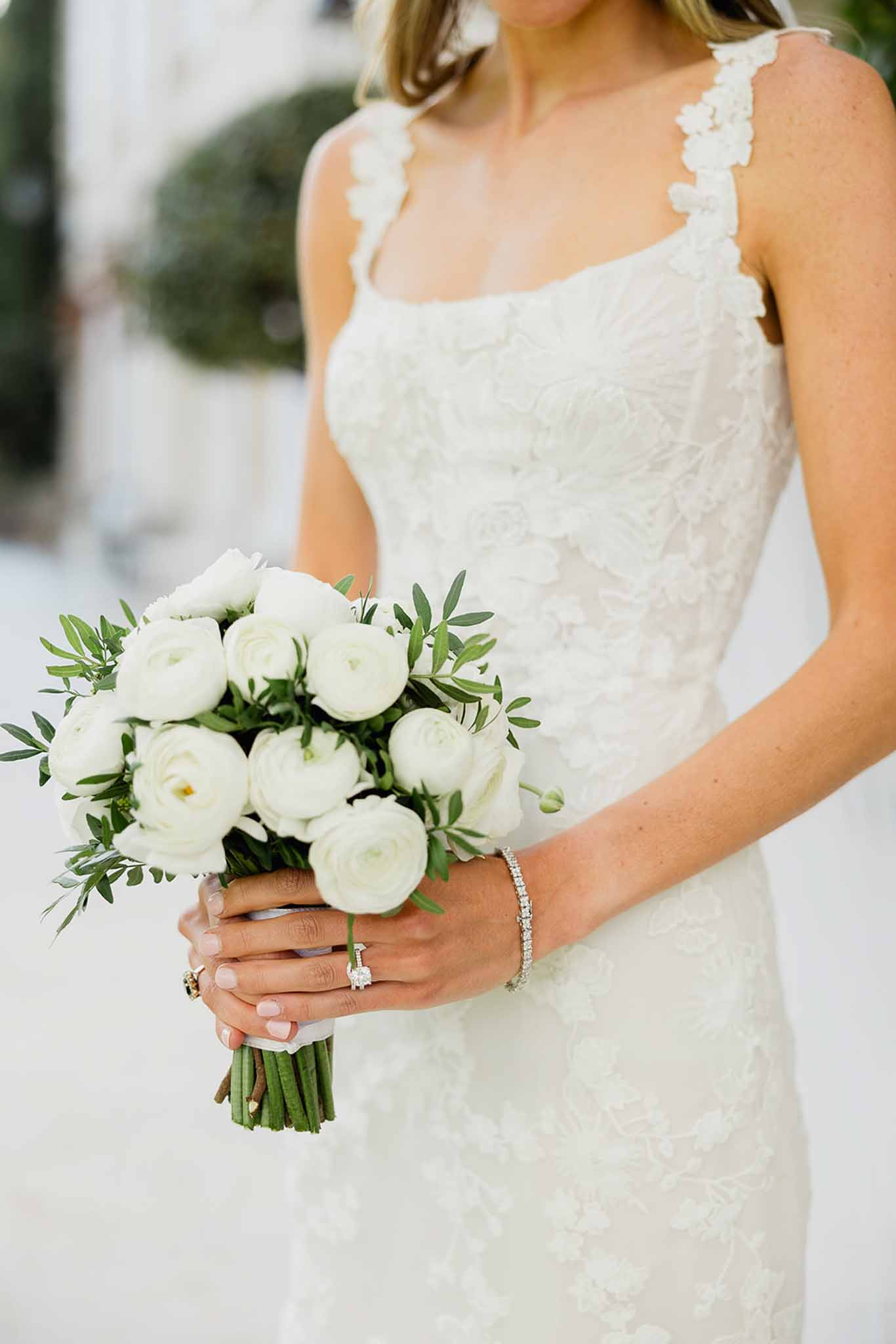 Bride holding white ranunculus bouquet in ivory lace wedding dress at outdoor venue