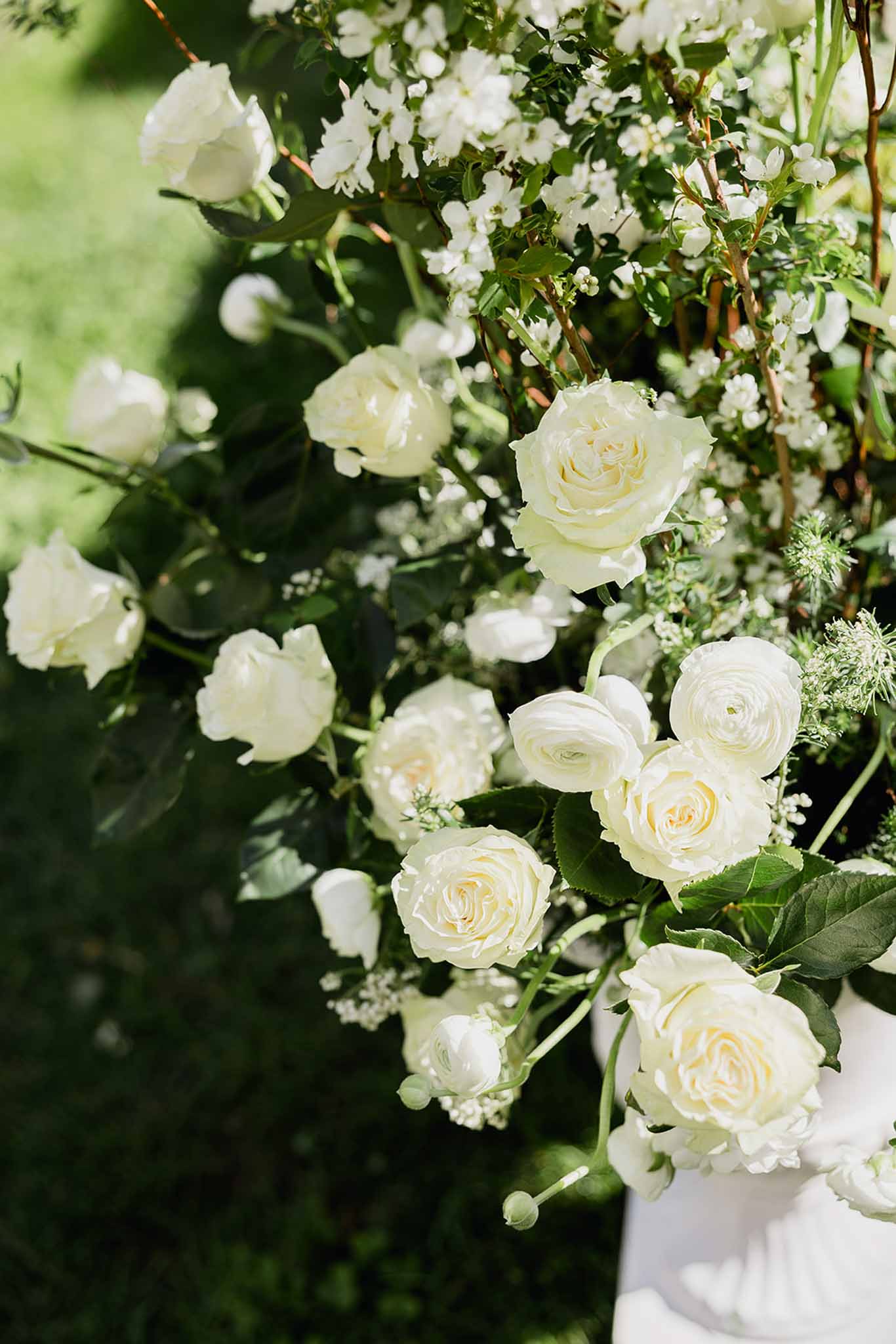 White and cream wedding floral arrangement with roses and ranunculus in ceramic vase